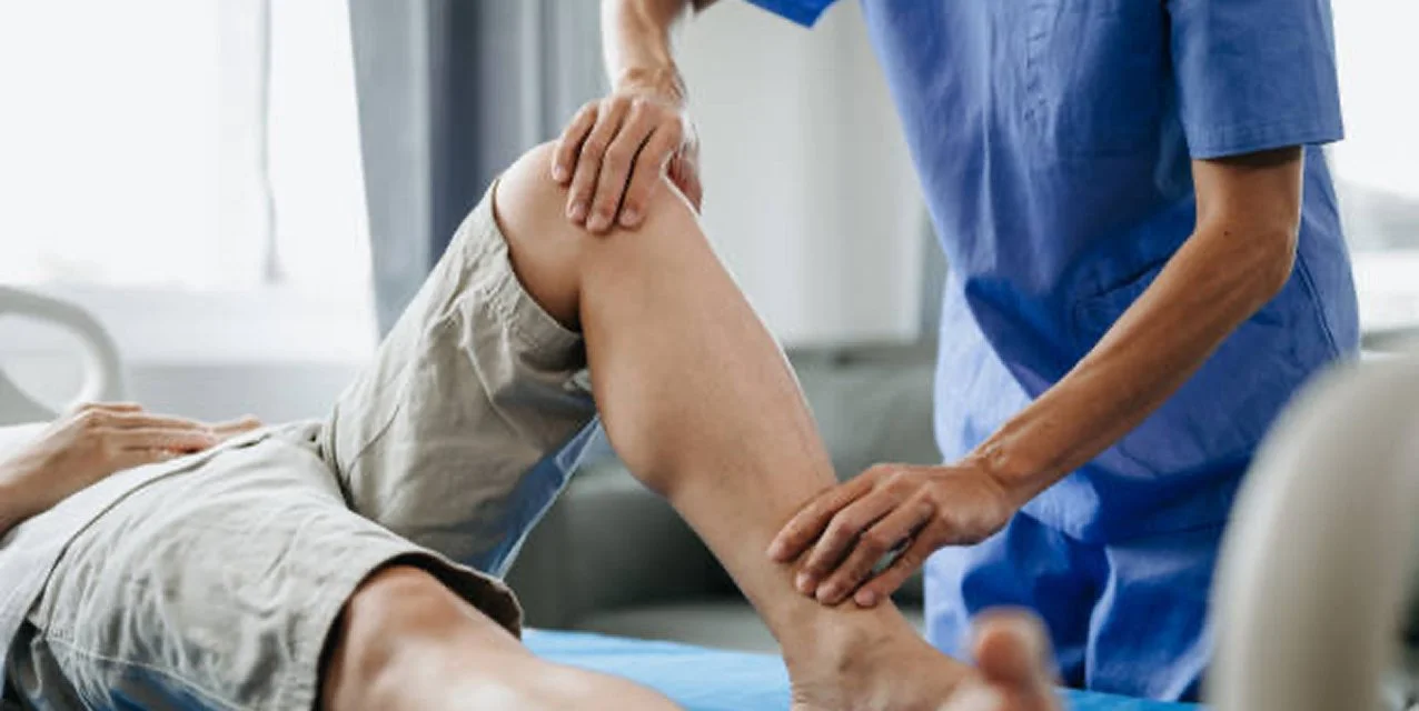 Healthcare professional examines patient's knee in a clinical setting.