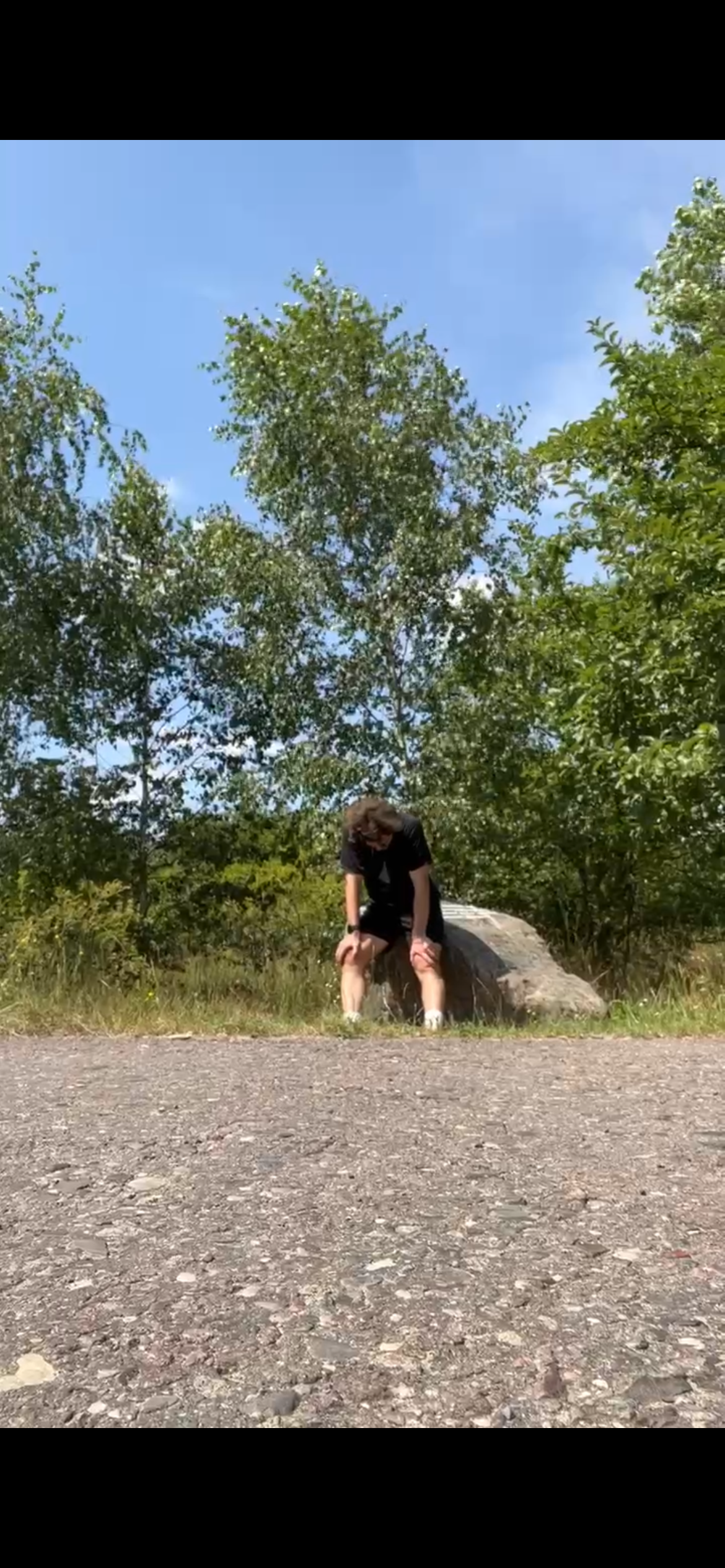 Ferdi Nees sitzt erschöpft auf einem Stein im Freien