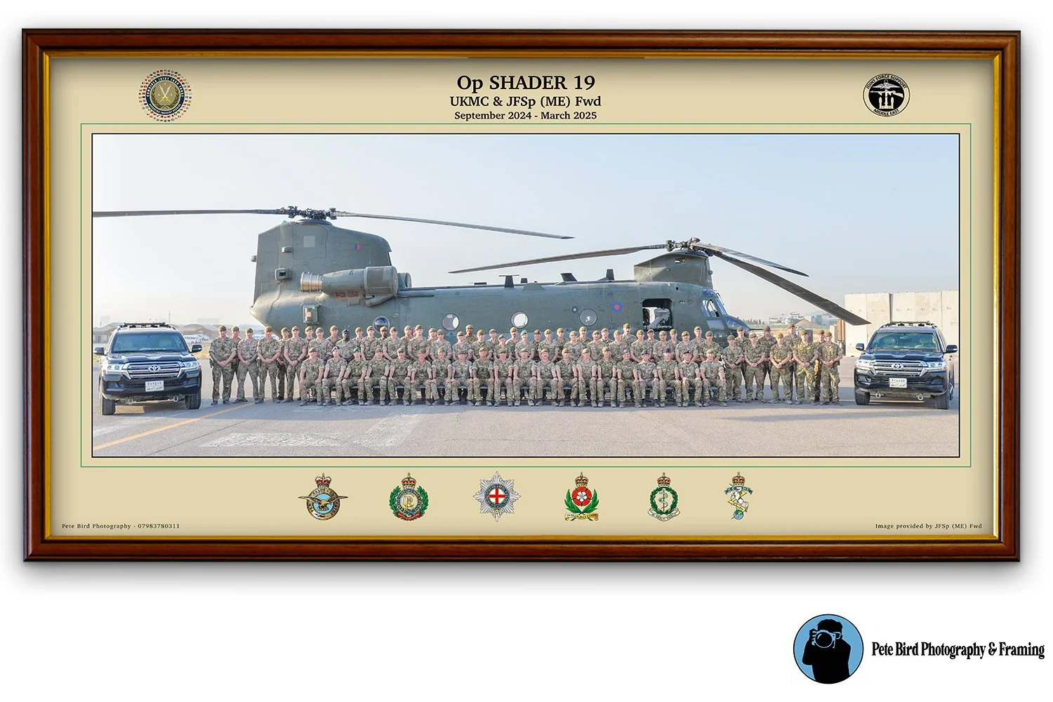 Group photo of soldiers and military vehicles, including a large helicopter and two black SUVs, taken outdoors on a tarmac with a framed military certificate or poster. The frame has military insignias and logos, with the title 'Operation Shader 19' and details about the troops and time period from September 2024 to March 2025.