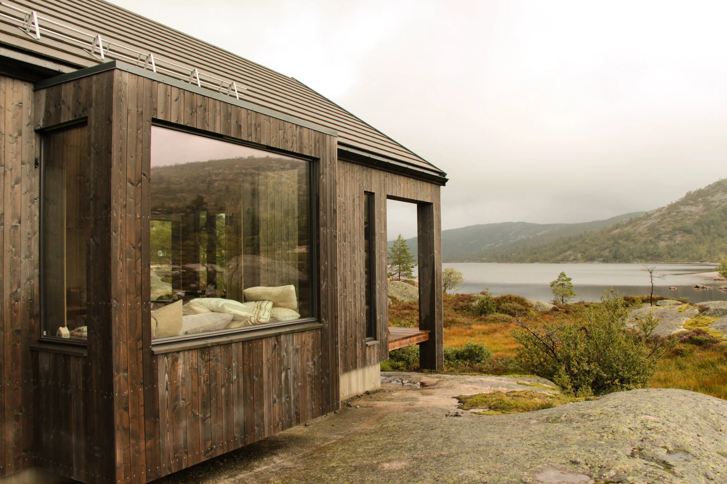 Fjellborg Hytter - Et hus med store vinduer ved en innsjø med fjell i bakgrunnen.