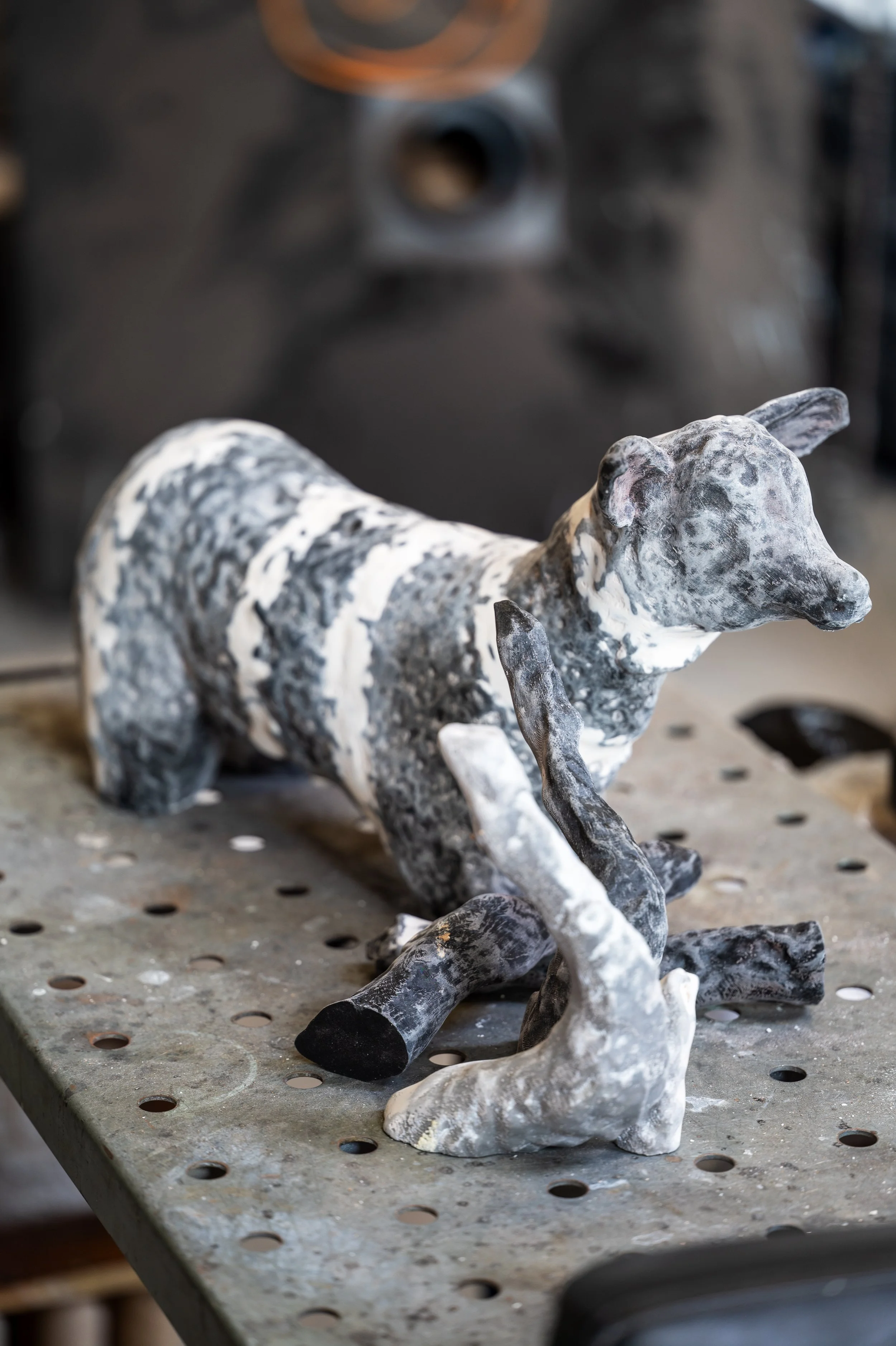 A ceramic sculpture of a dog, predominantly black and white with a marbled pattern, placed on a workbench.