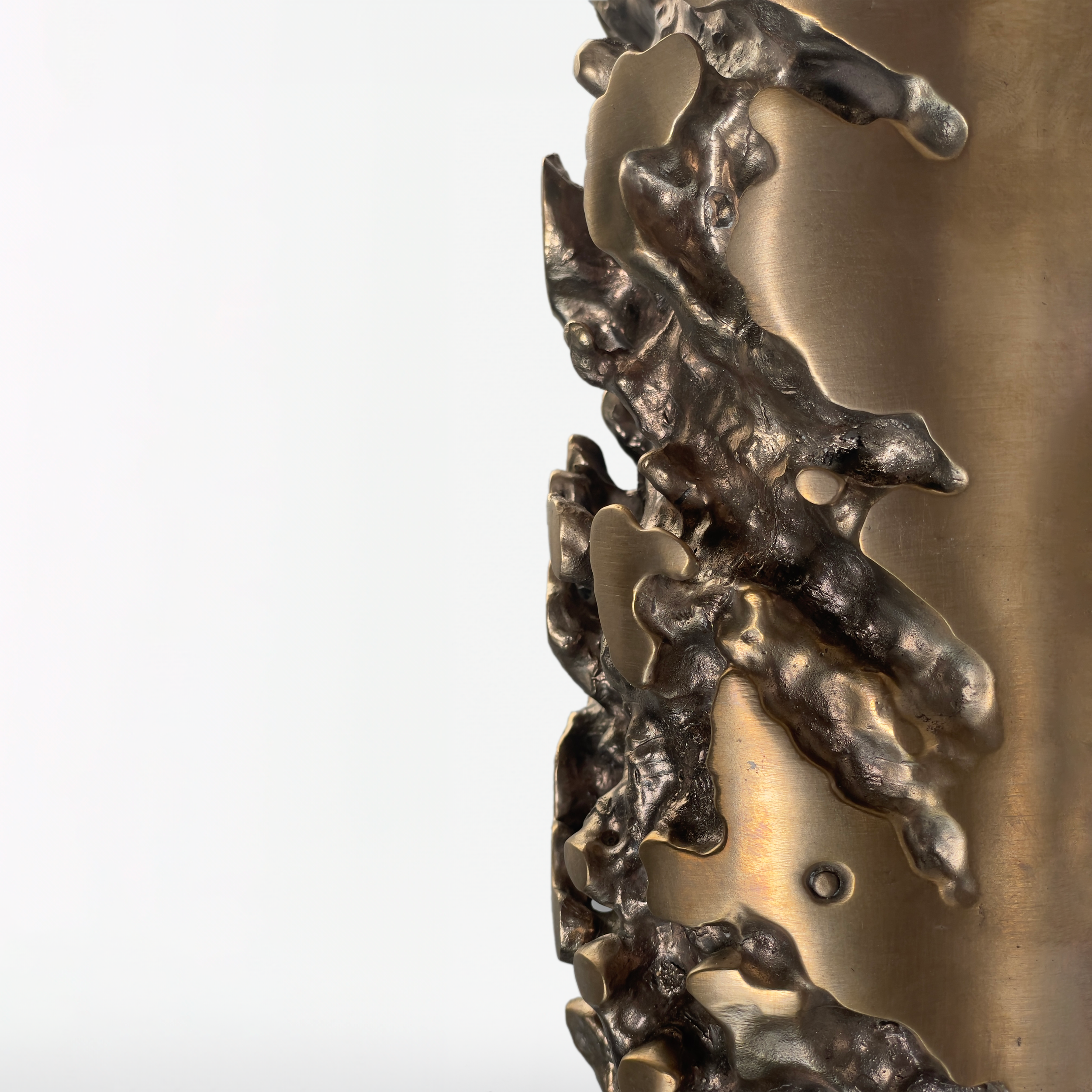 Close-up of an abstract metal sculpture with textured, irregular surfaces and smooth, curved areas, set against a plain white background.