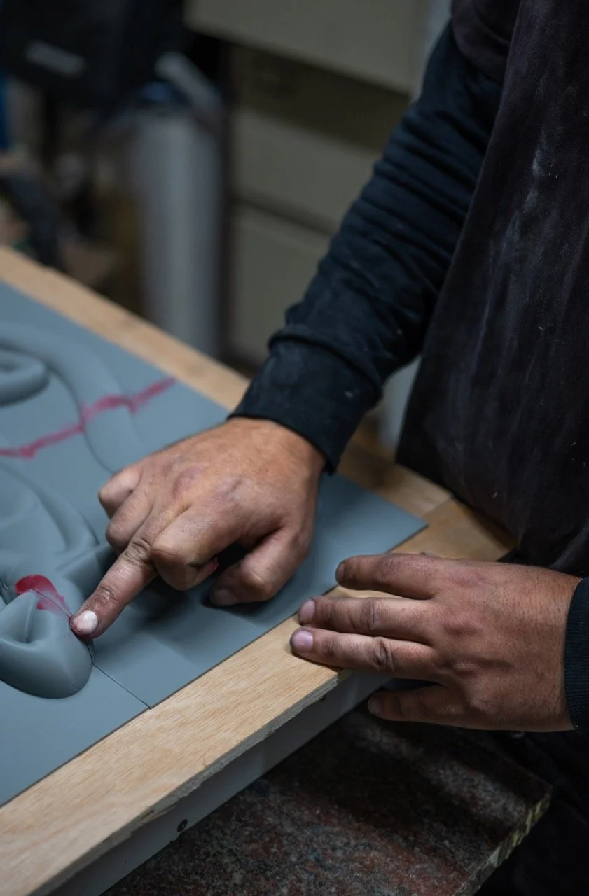 Person working on a gray, molded clay sculpture on a wooden workbench.