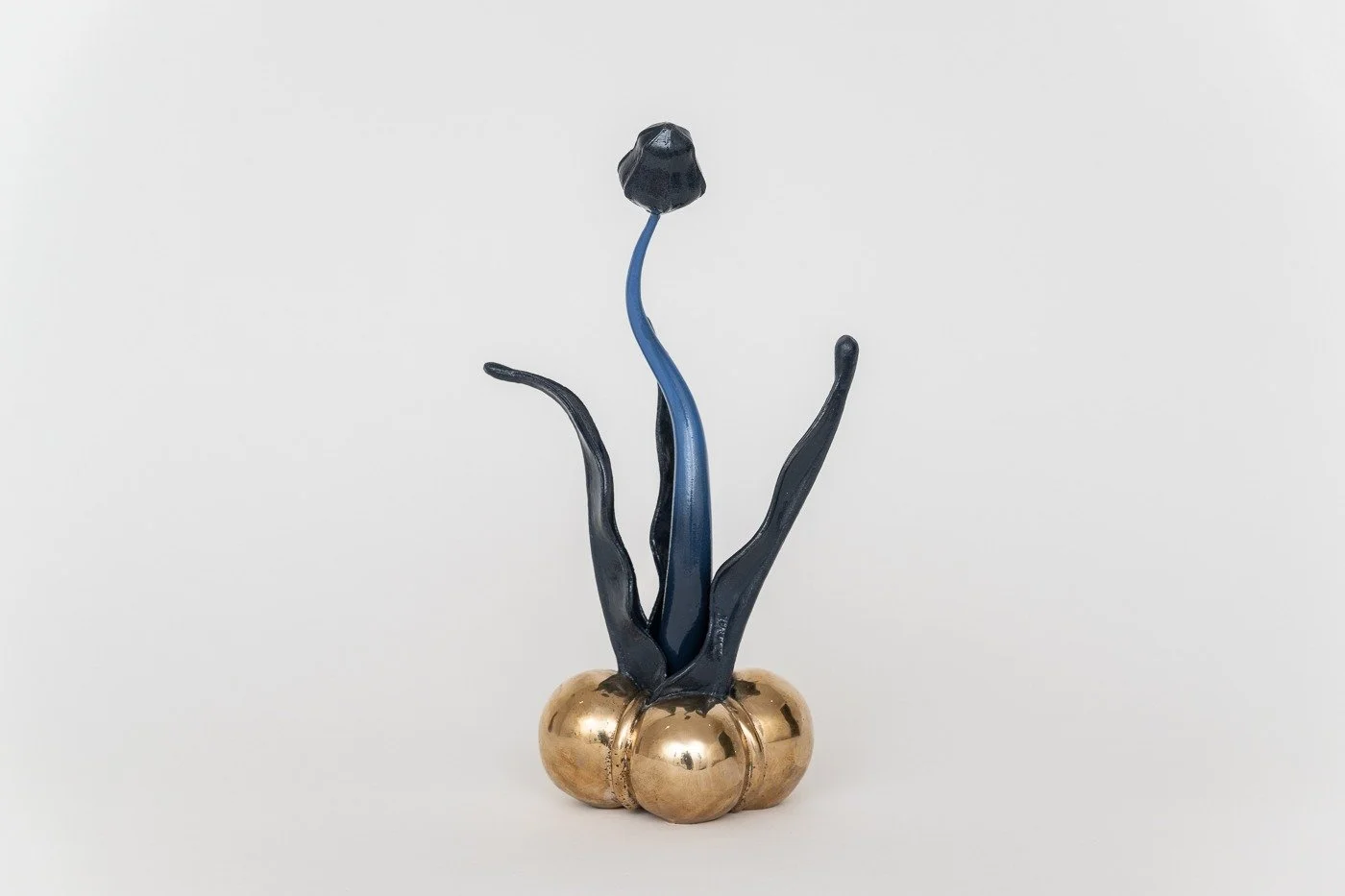 A decorative art sculpture resembling a plant with a black flower on a blue stem and dark curves emerging from a gold base.