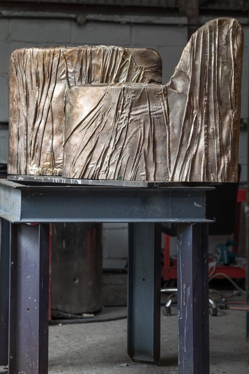 Close-up of a bronze sculpture with textured, vertical lines, placed on a metal stand in a workshop setting.