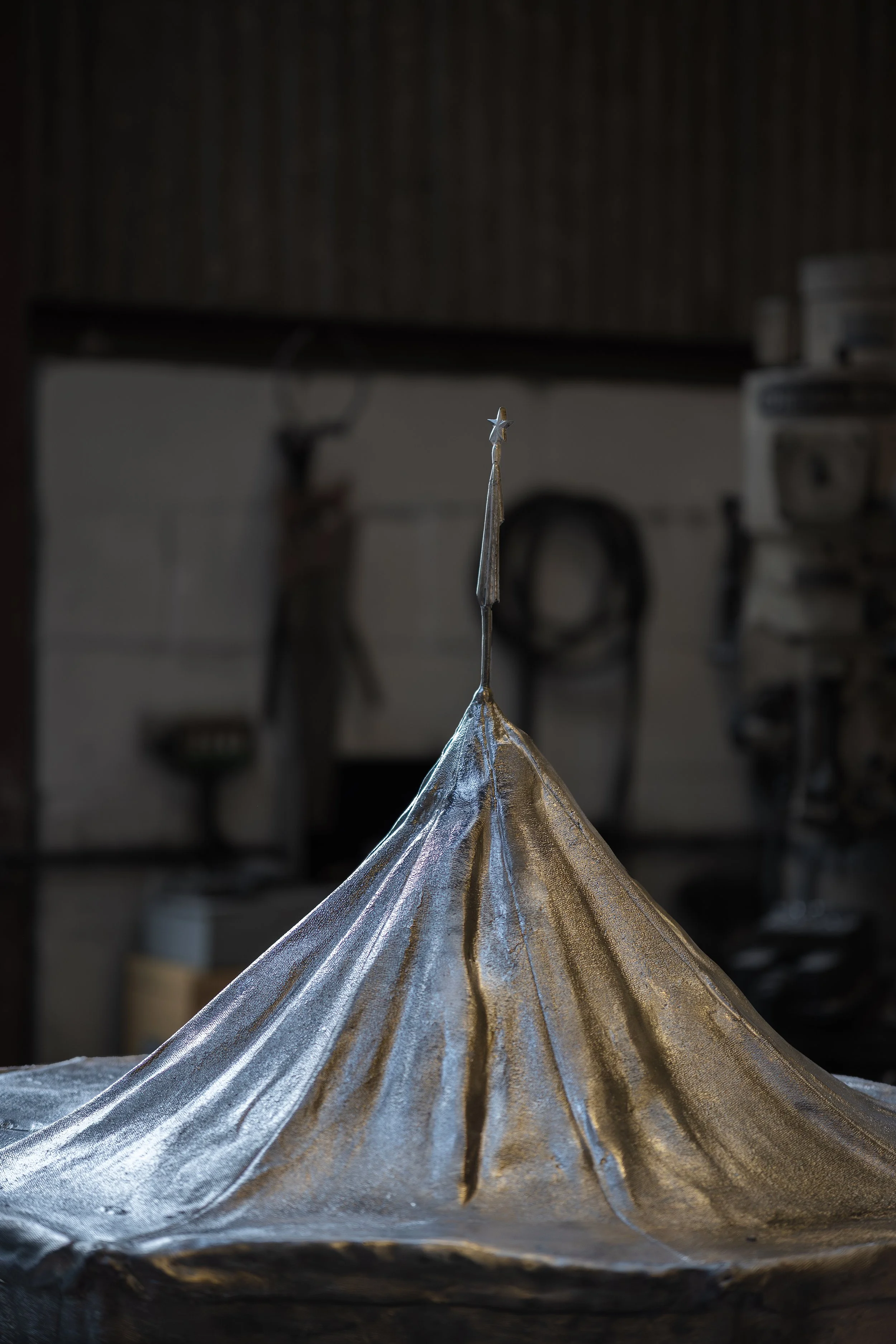 A metallic model of a conical mountain with a star on top, set in a workshop or studio.