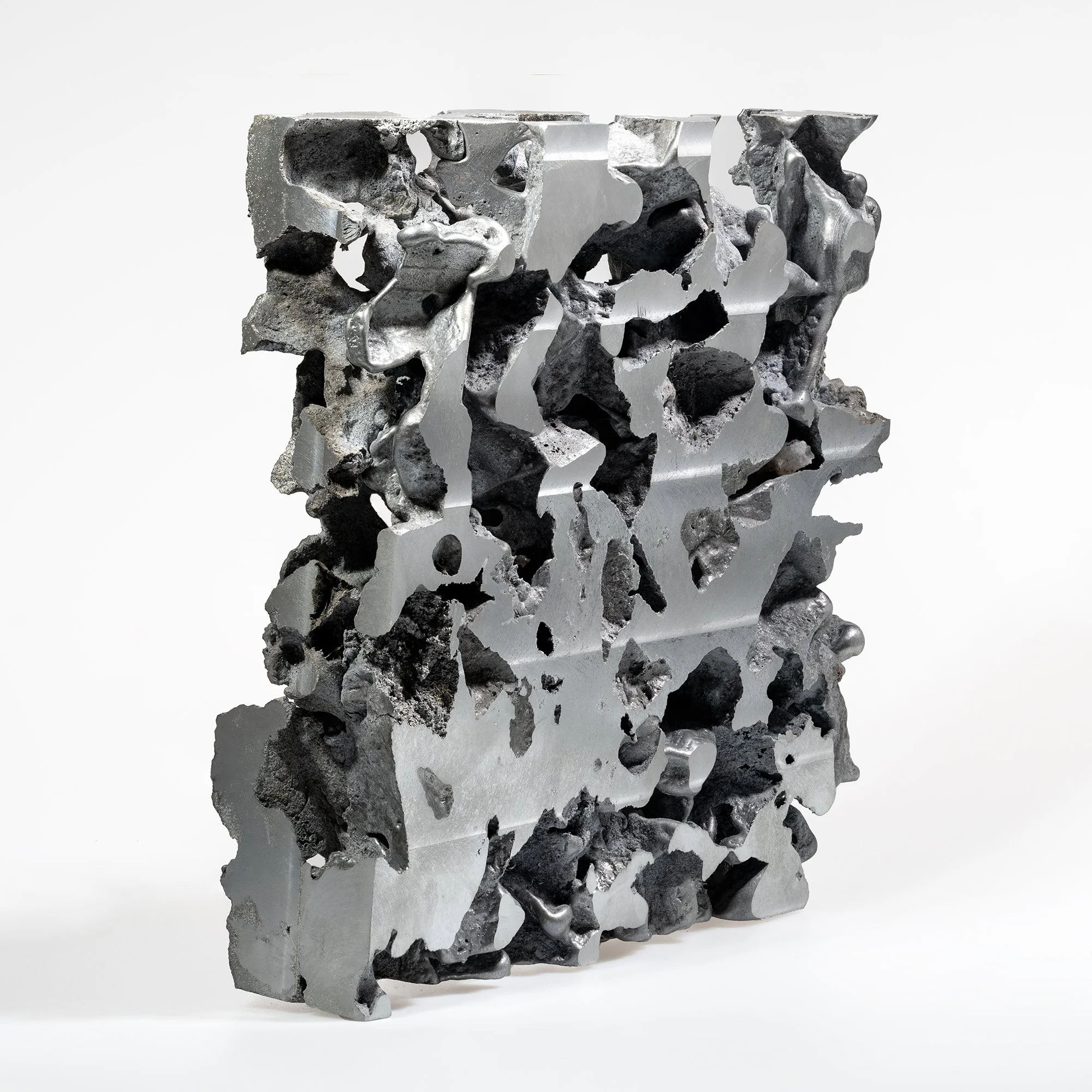 An abstract sculpture made of mixed metallic and rocky materials with an open, irregular design and a predominantly gray and black color scheme.