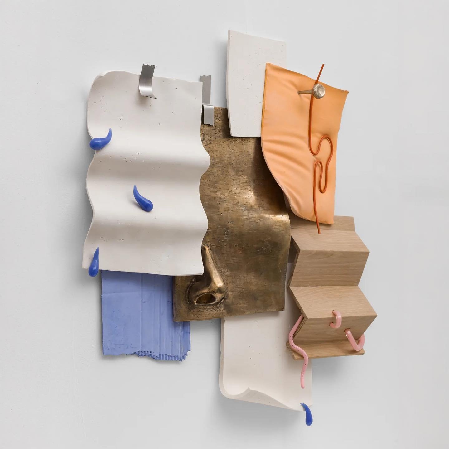 Mixed media art piece with various textures and materials including wood, metal, fabric, and plastic, arranged abstractly on a white background.