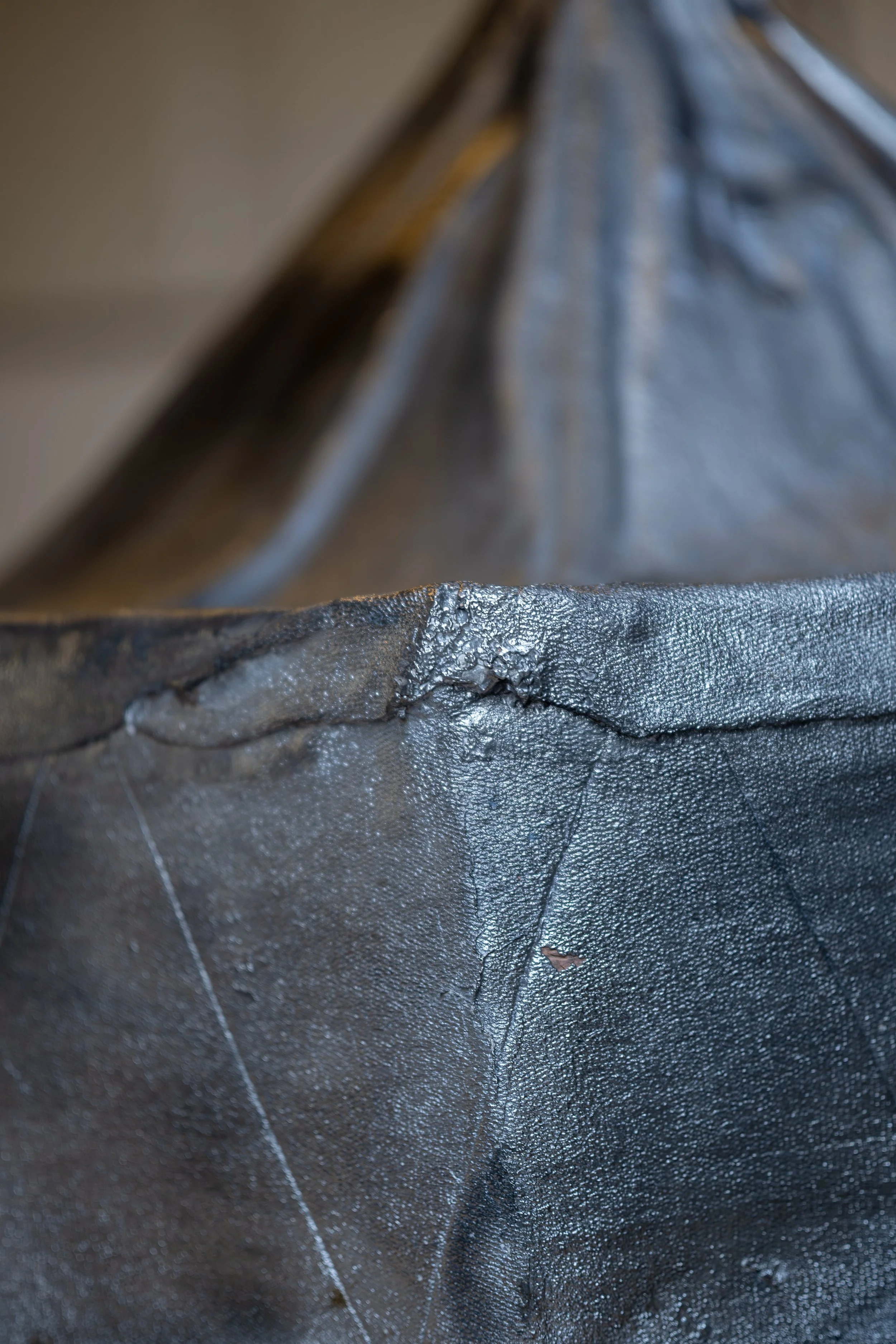 Close-up of a damaged black plastic or fabric bag with a tear and some surface cracks.