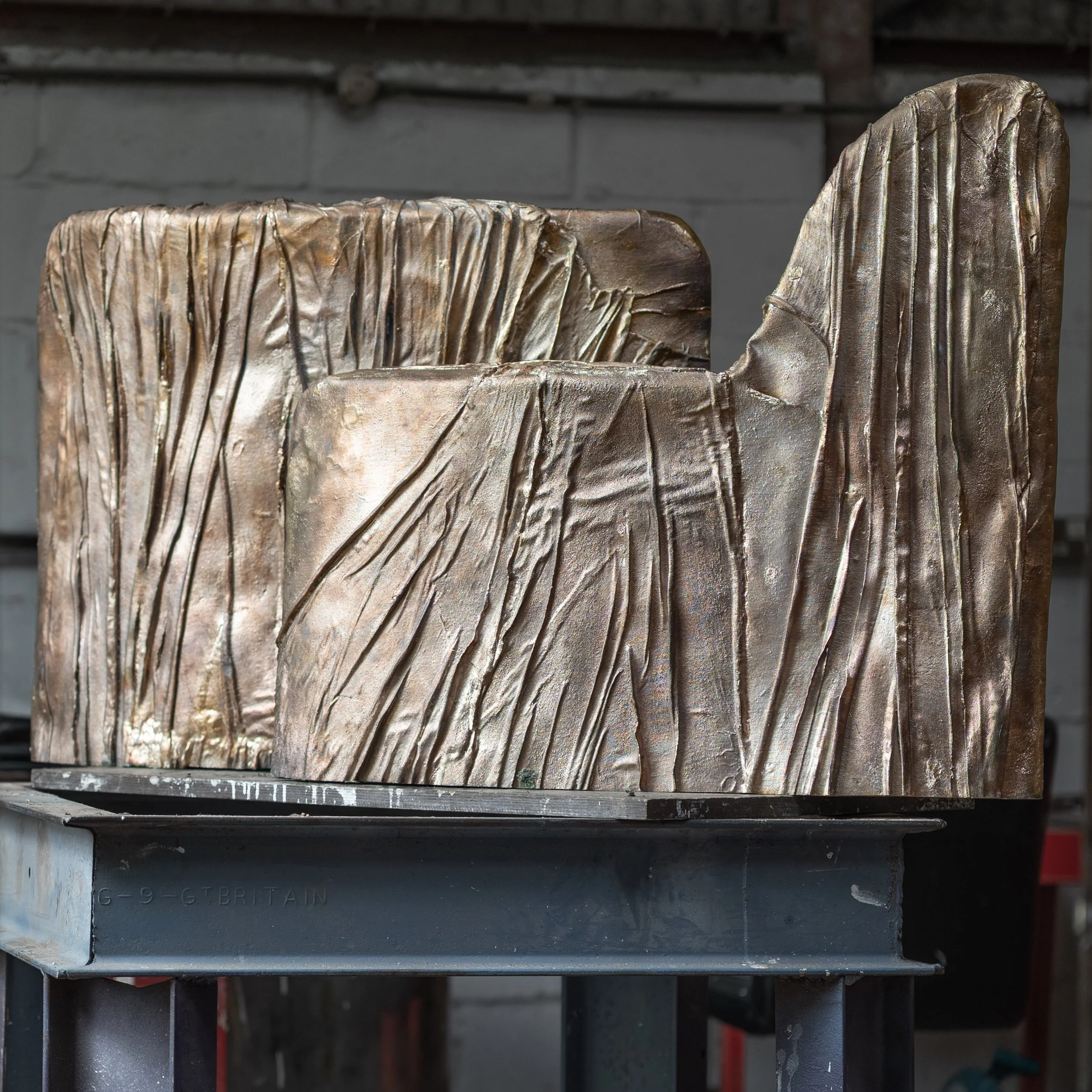 Two bronze sculptures with textured, abstract designs are placed on a metal platform in an indoor setting.