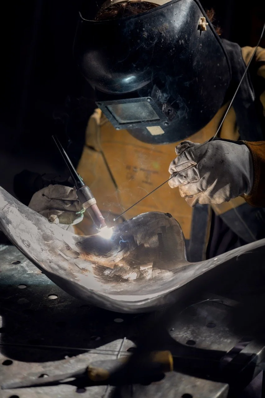 Welder wearing safety gear welding a metal piece.