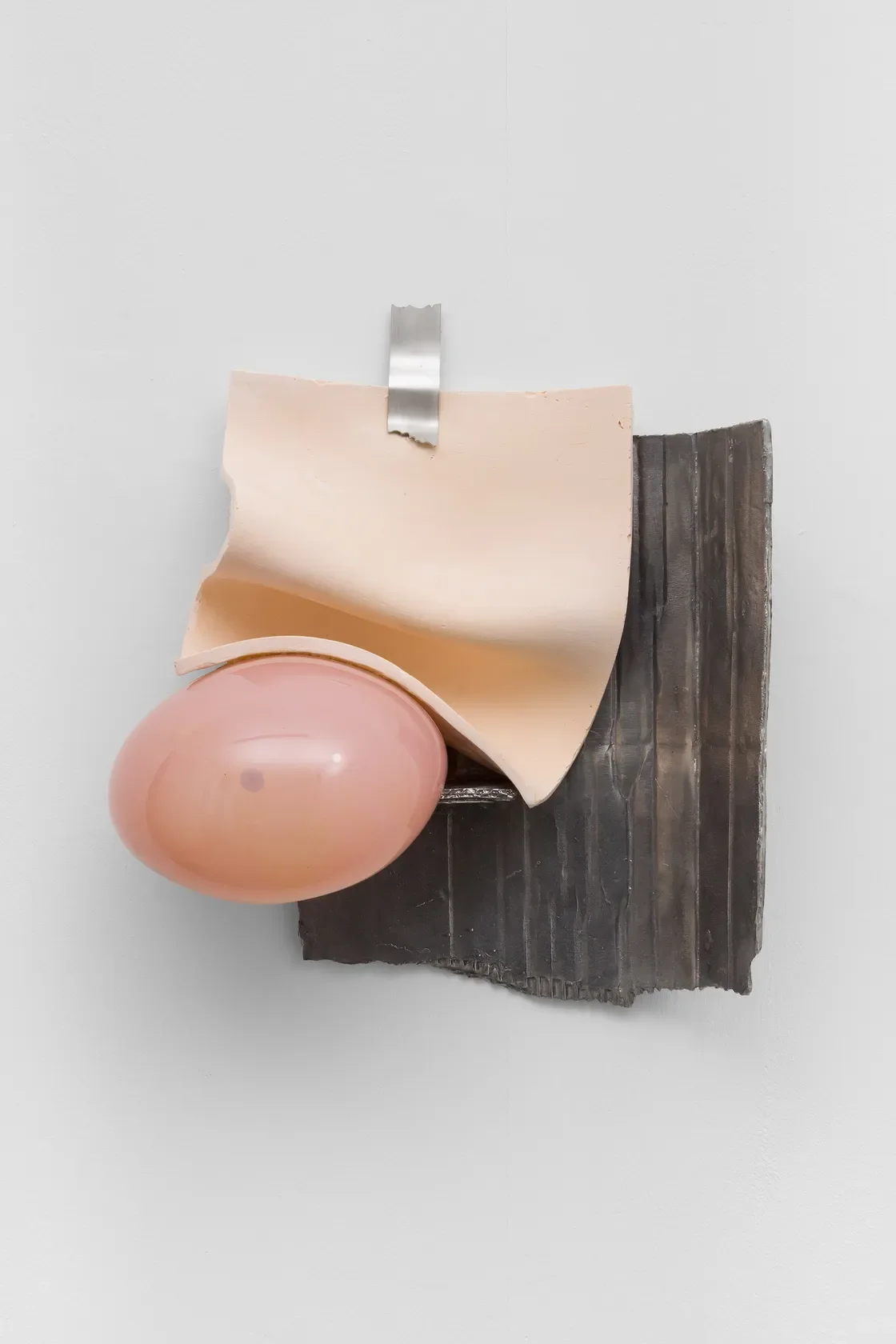 Object that resembles a model of a human uterus with a pink egg-shaped form inside, placed on a black base and taped to a white background.