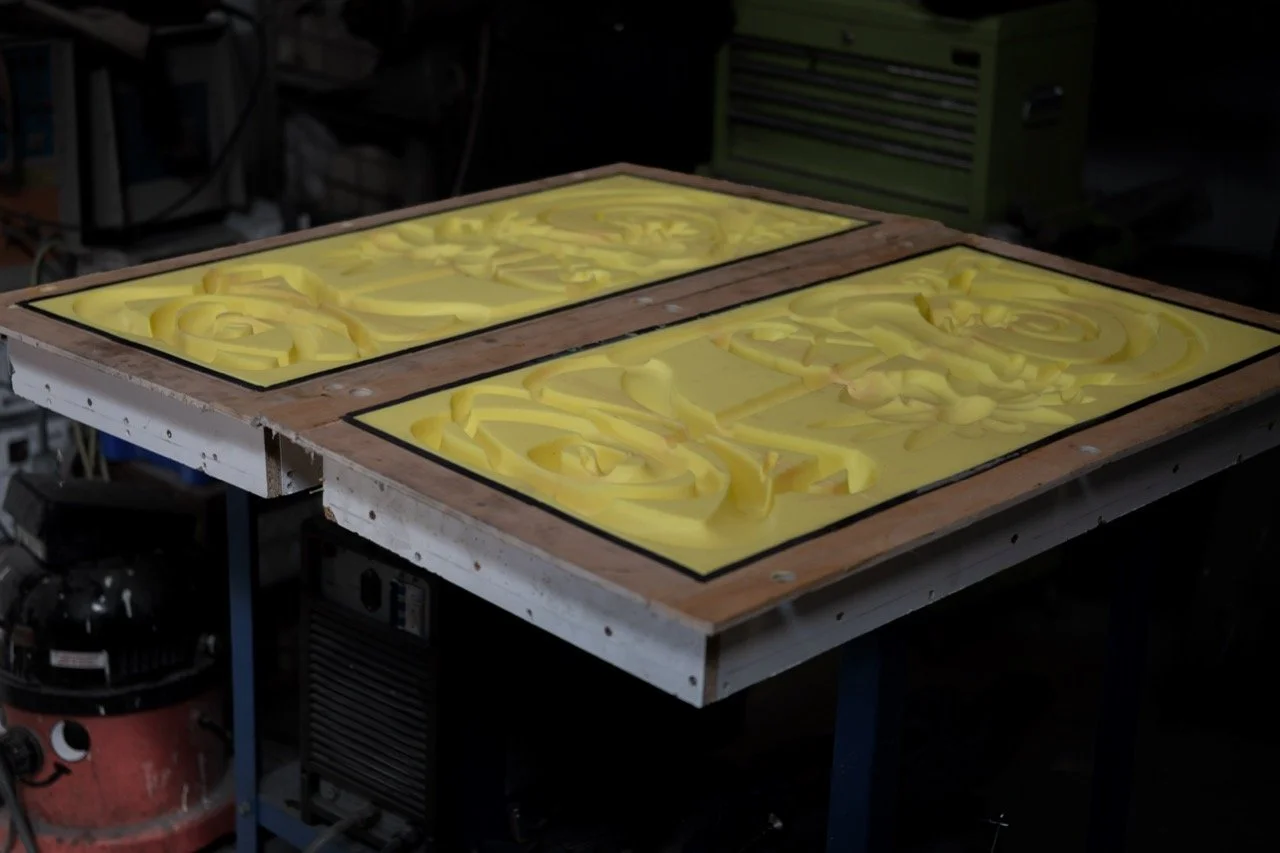 Two glass panels with yellow soap or wax strips laying on a wooden frame, placed on a workbench in a workshop.
