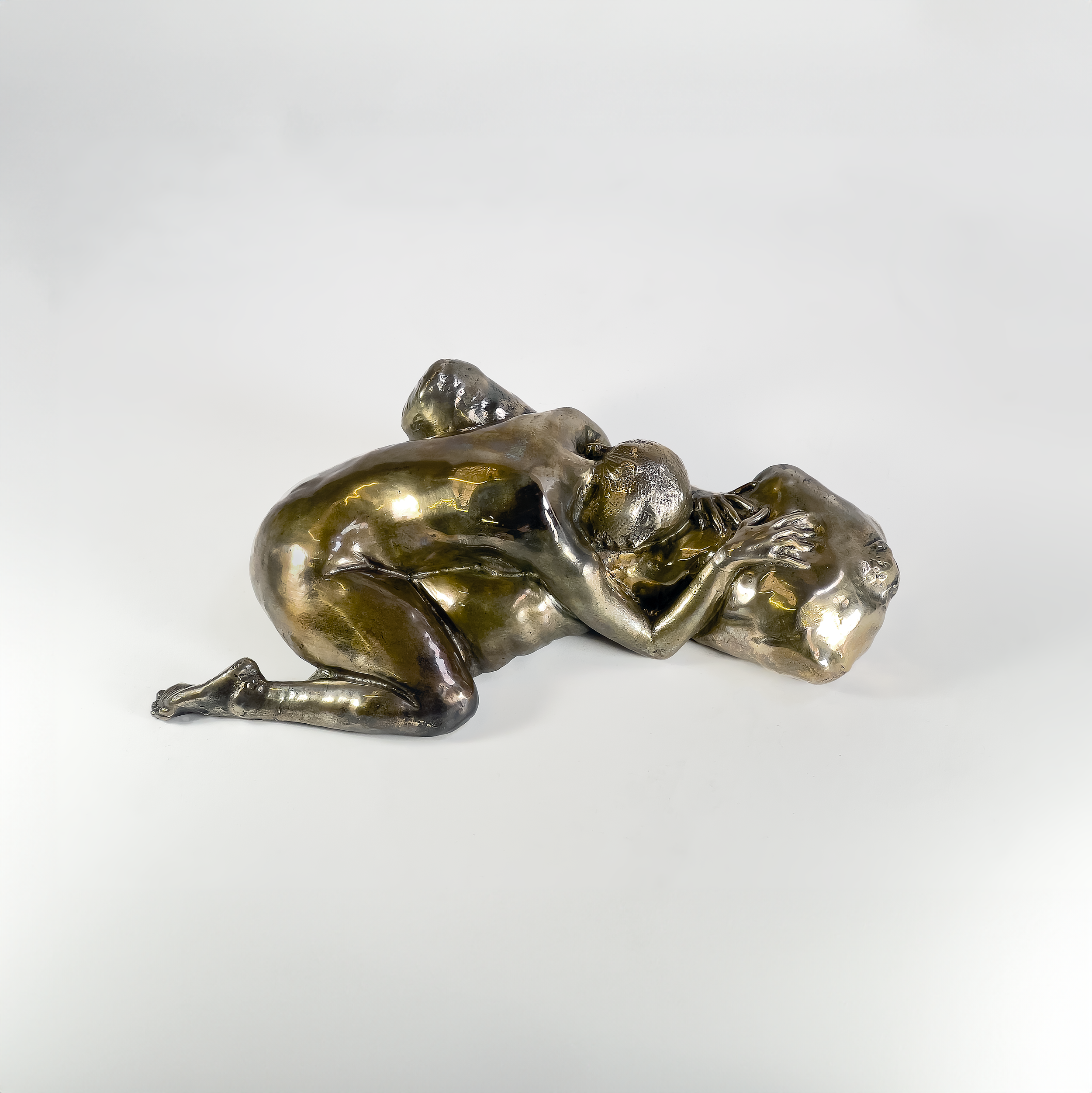 Bronze sculpture of two figures embracing, with one figure lying on top of the other, both with their eyes closed and limbs intertwined.