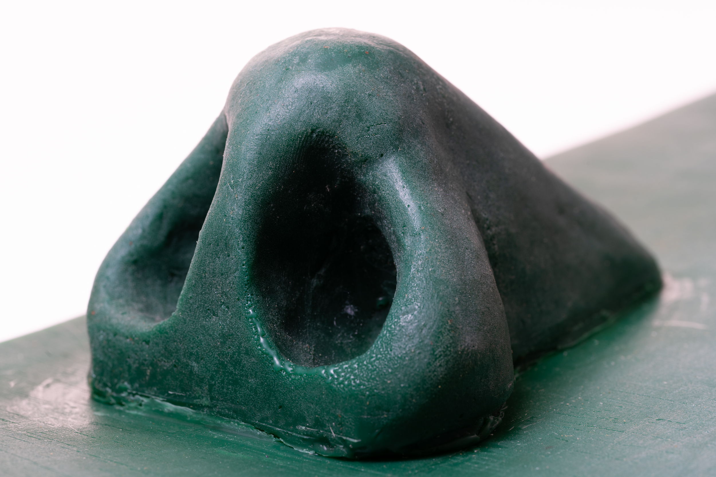 Close-up of a dark green, textured crafting wax sculpture with hollow centers, placed on a wooden surface.