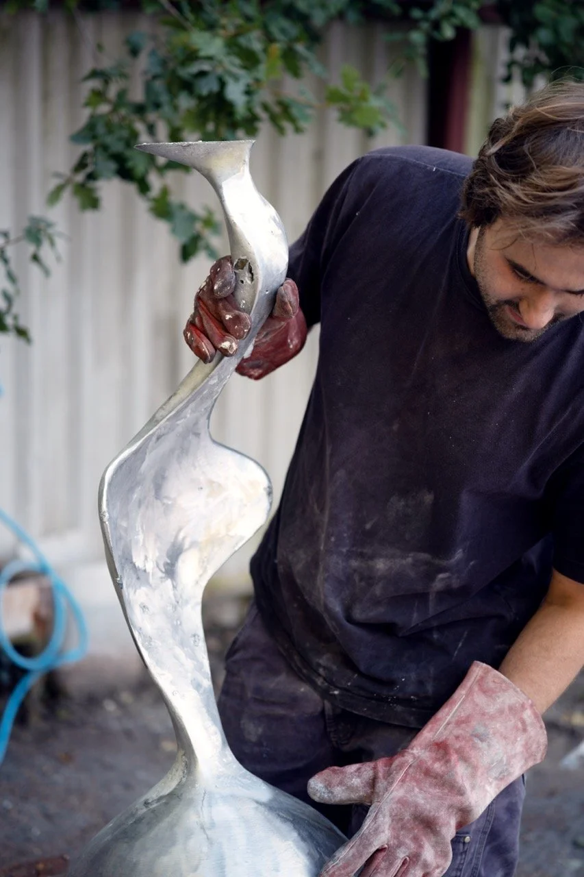Man wearing black shirt and red gloves holding a modern, abstract metal sculpture outdoors.