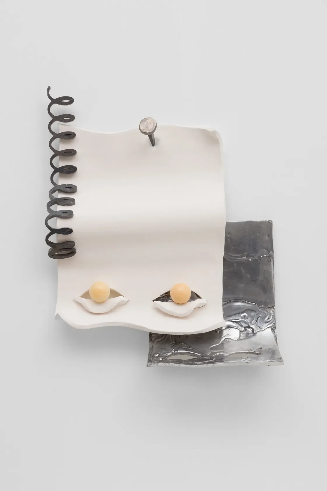 An abstract art piece featuring a piece of crumpled white paper, two yellow balls, and various metallic elements, arranged on a flat surface with a minimalist aesthetic.