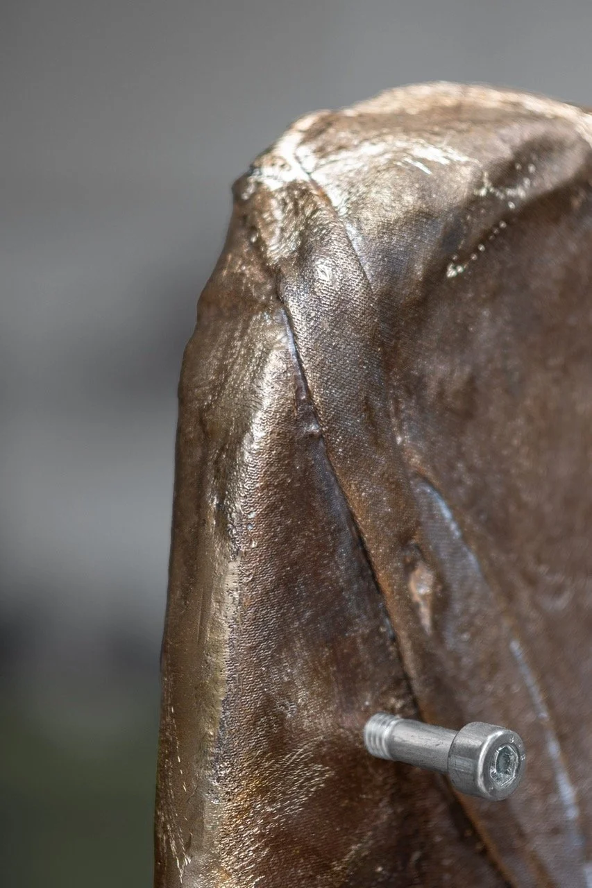 Close-up of a brown, textured statue with a metallic bolt attached near the bottom.
