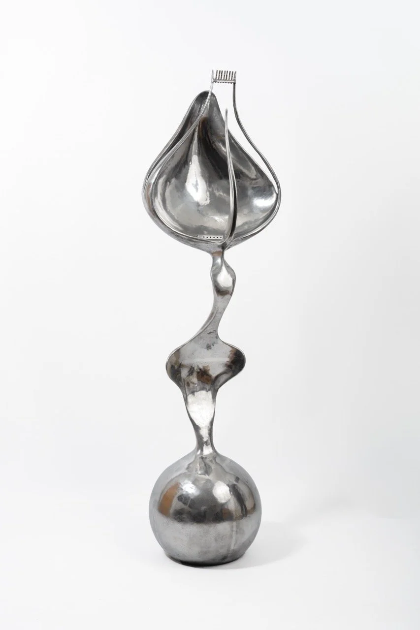 An abstract modern sculpture made of shiny silver metal with a spherical base, a thin elongated middle section, and a bulbous top, against a plain white background.
