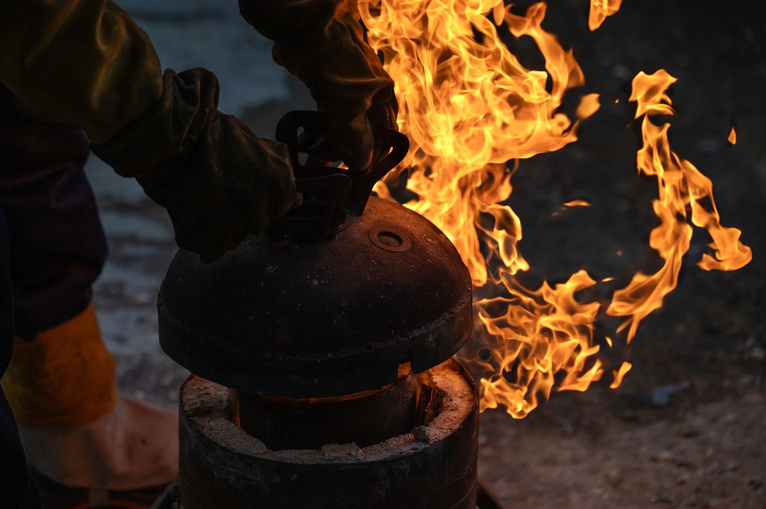 Person holding a metal object over a fire, with flames rising around it.