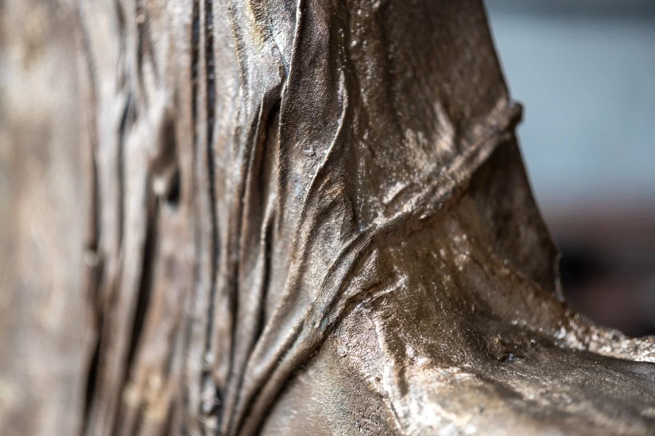 Close-up view of a bronze or metallic sculpture with detailed textures and folds.