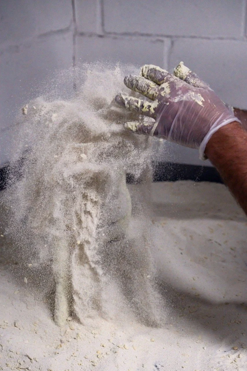 A person wearing a glove is hitting a clay sculpture, causing dust and debris to fly.