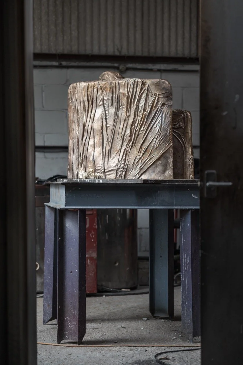 A bronze sculpture on a black metal table in a workshop, with a concrete wall in the background.