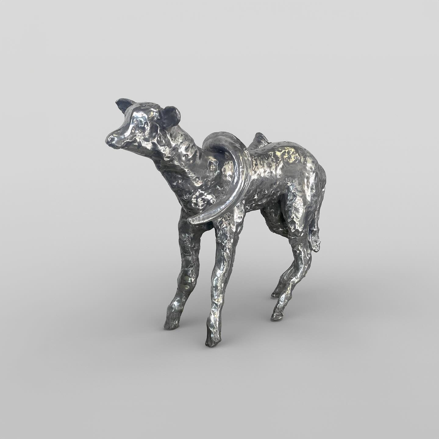 A silver metallic sculpture of a dog with a curved tail standing on a plain background.