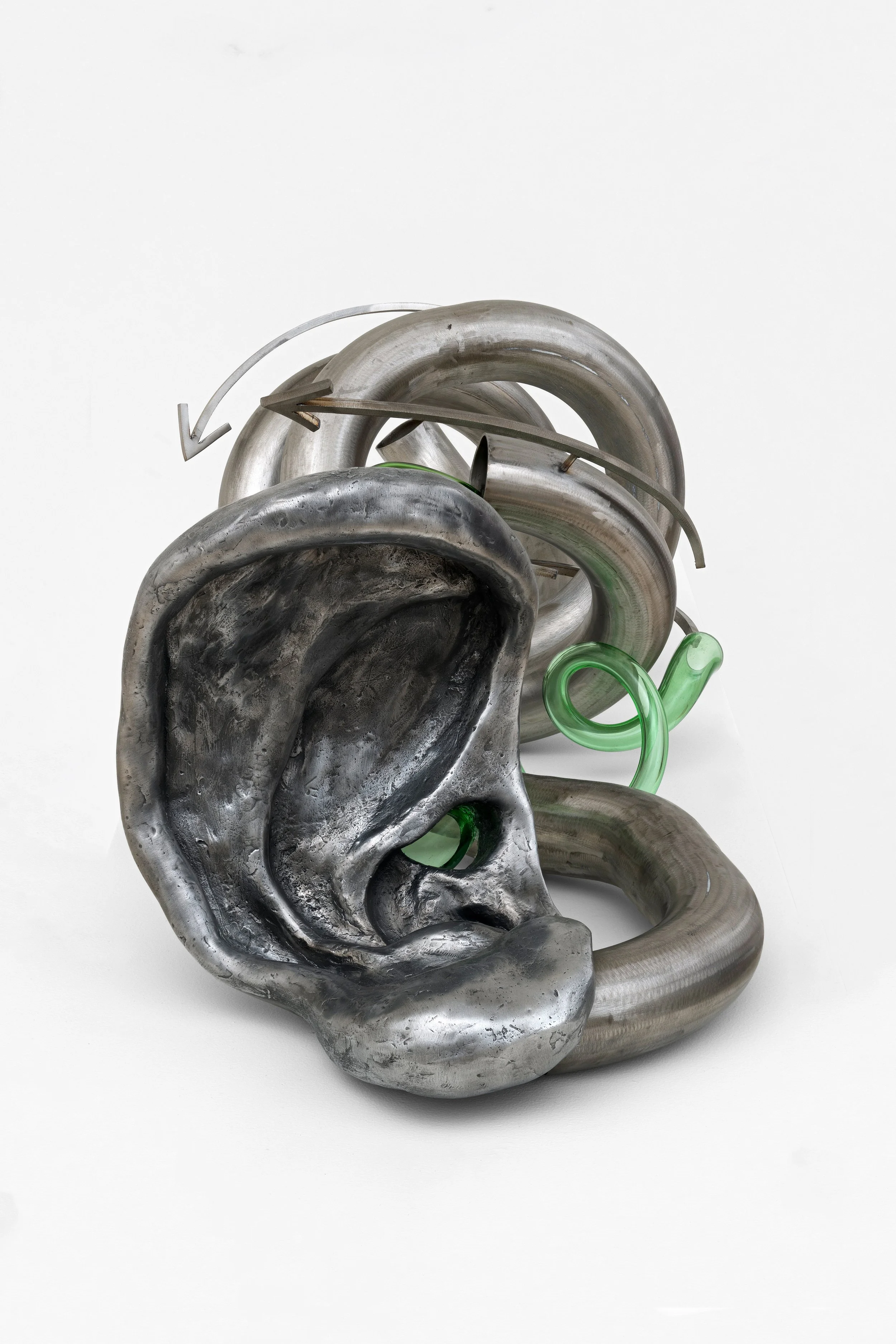 A mixed media sculpture of a human ear and a coiled tube, made of metal and green glass, displayed against a plain white background.