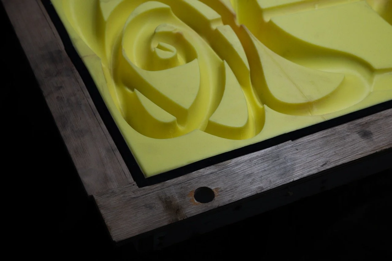 Close-up of a yellow rubber mold with carved rose designs, placed on a wooden board.