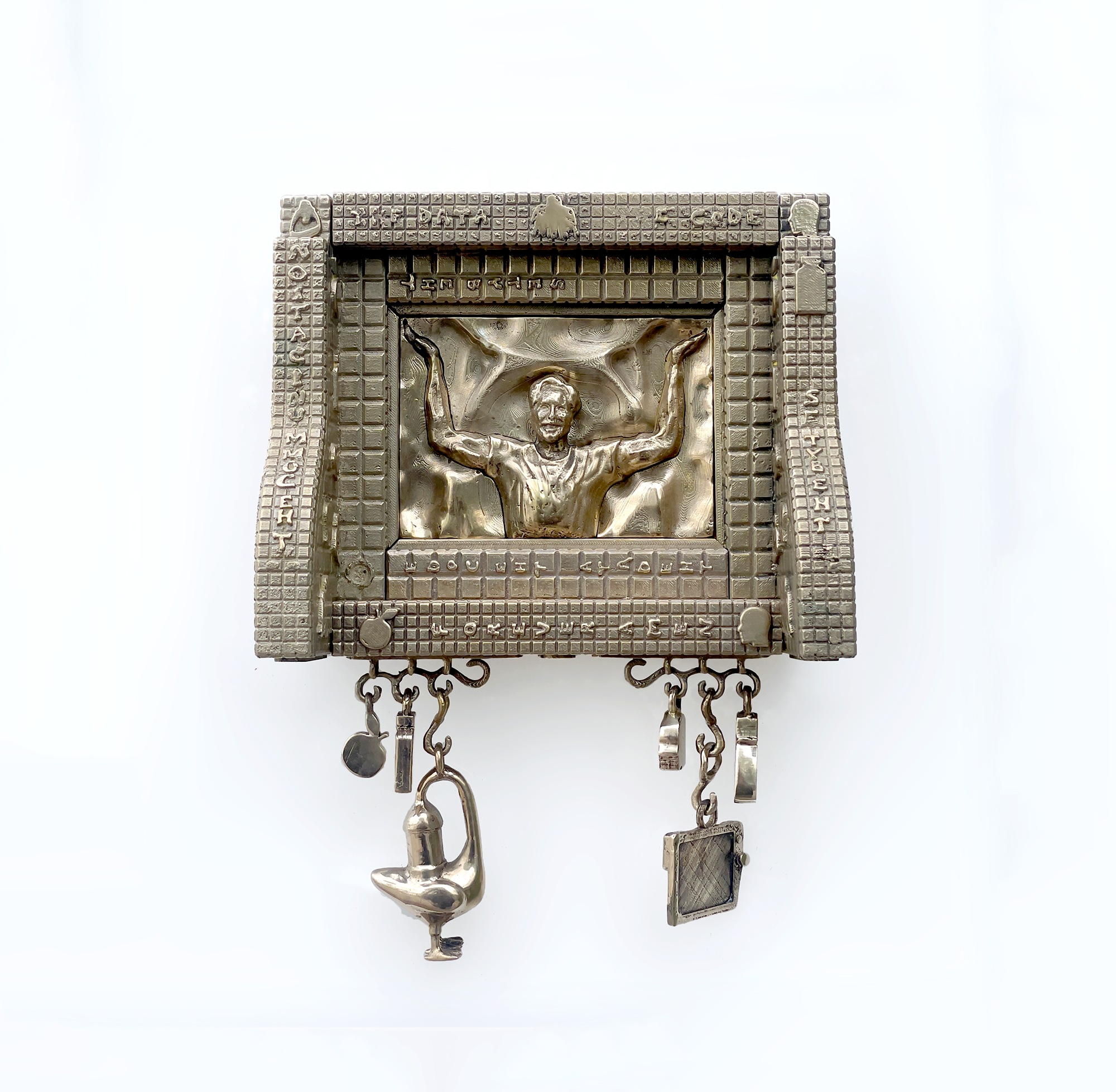 A metallic sculpture of a man with arms outstretched, surrounded by a textured square frame with engraved text. Several small hanging charms and objects dangle from the bottom.