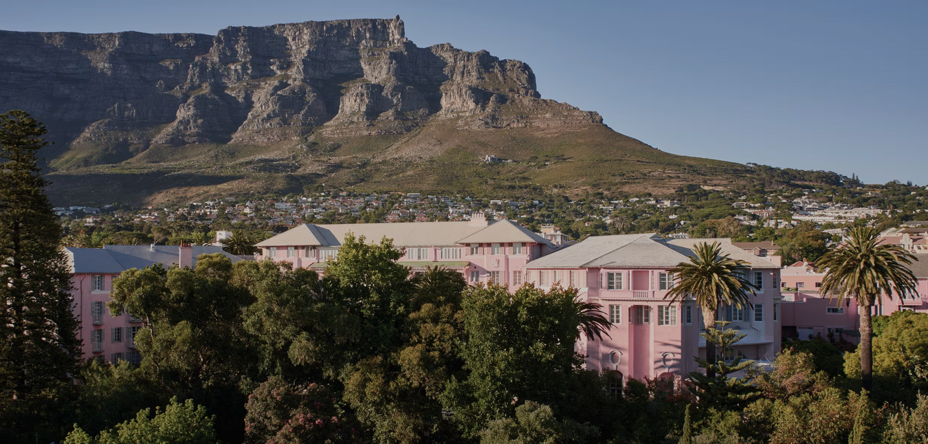 Mt. Nelson, residential buildings surrounded by trees with Table Mountain in the background under a clear sky.