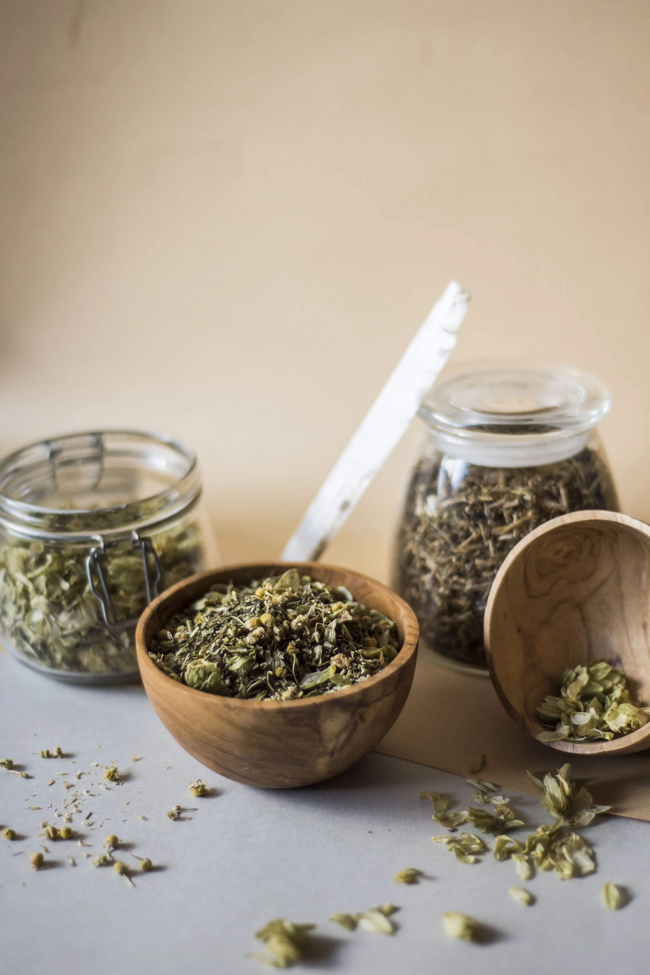 Various jars and bowls filled with dried herbs and flowers on a white surface, with some herbs spilled around.