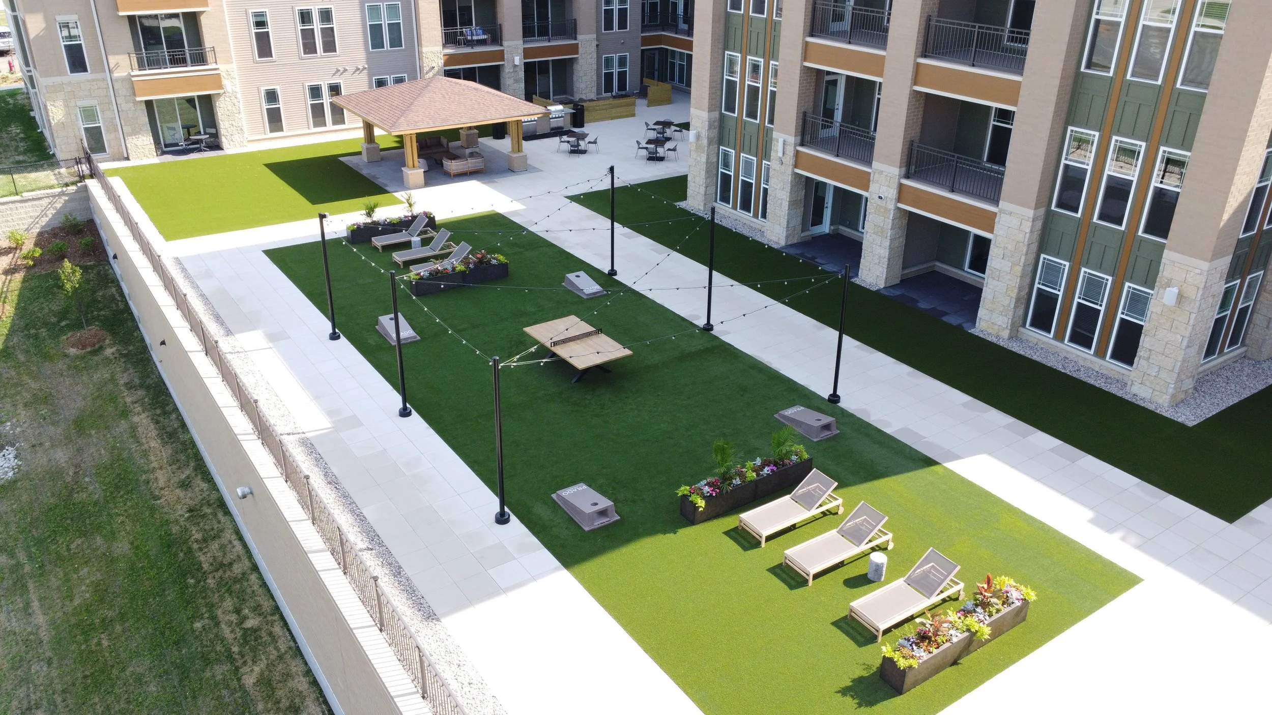 Aerial view of an apartment complex courtyard with seating, flower beds, a pavilion, and artificial grass areas.
