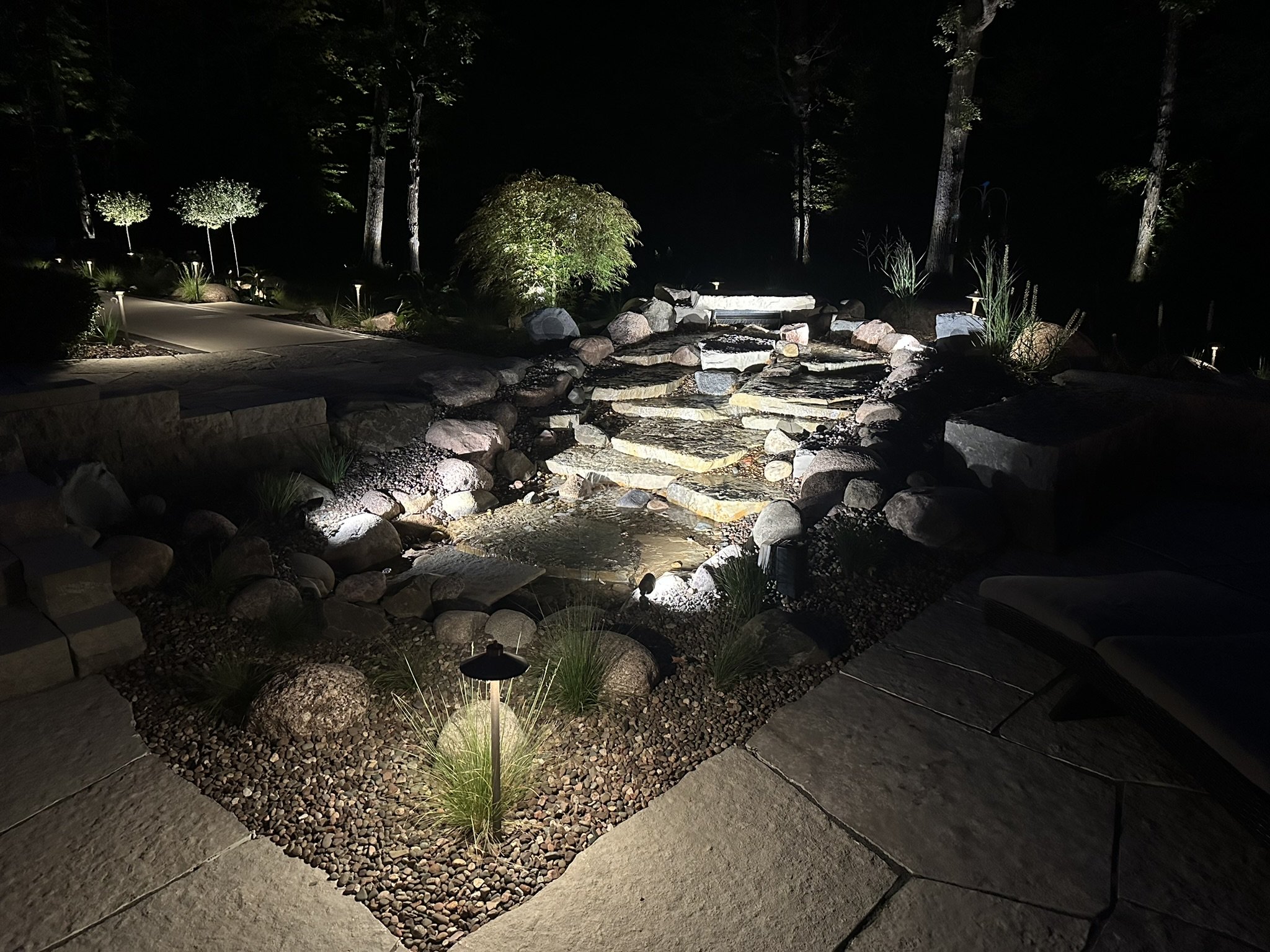 Backyard waterfall lit by low-voltage landscape lighting after dark in Menomonee Falls, WI