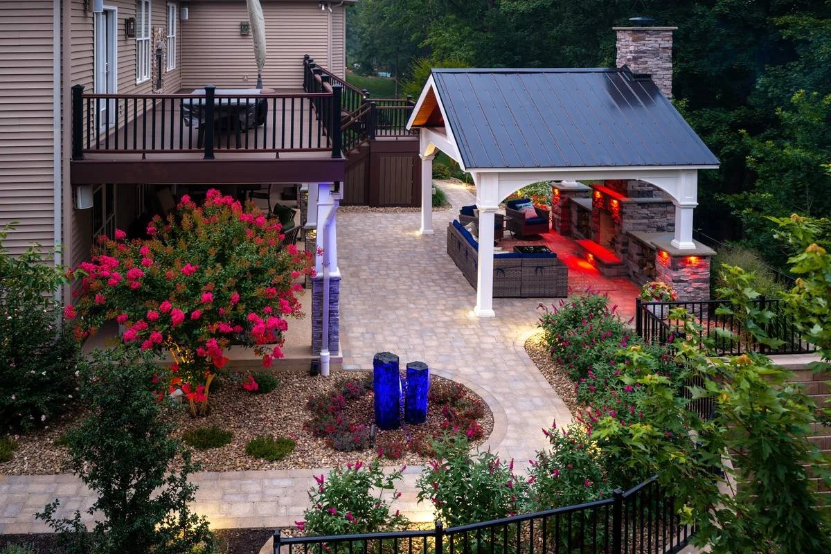Backyard patio at dusk with red ambient lighting on the fireplace and a blue-lit water feature — GoldGlo Landscapes
