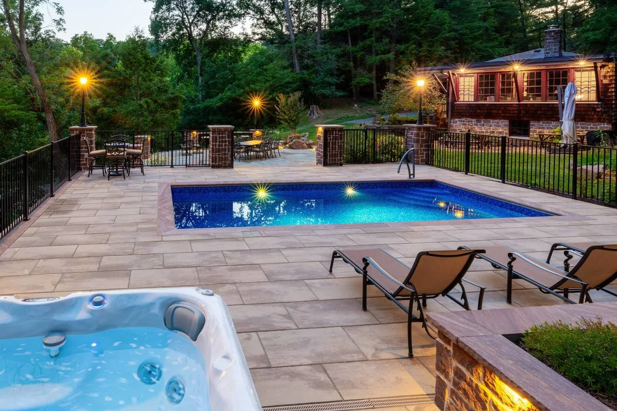 Inground pool with a large-format paver deck, spa, and lounge chairs at dusk — GoldGlo Landscapes