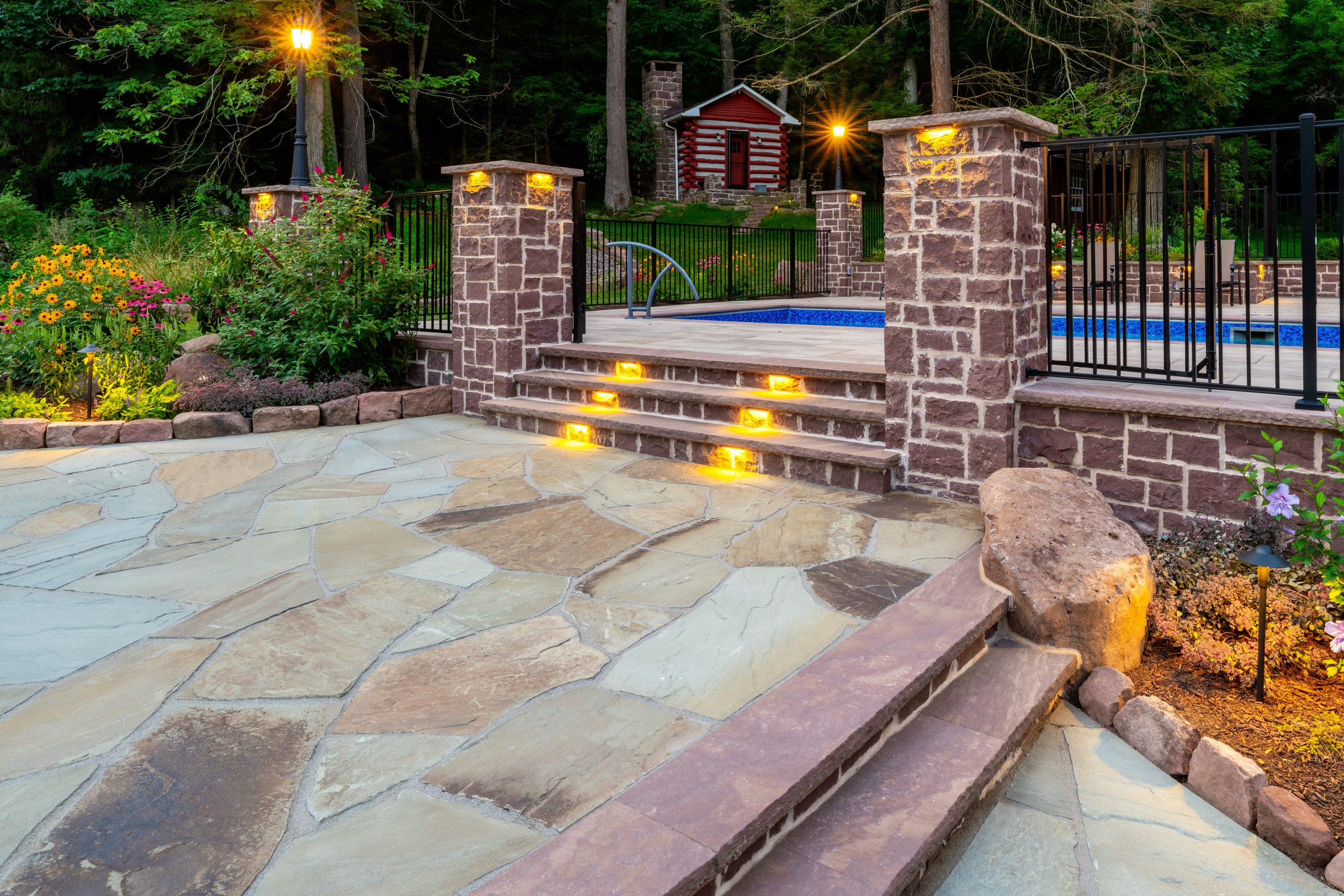 Lit stone steps between stone pillars leading to a pool area.