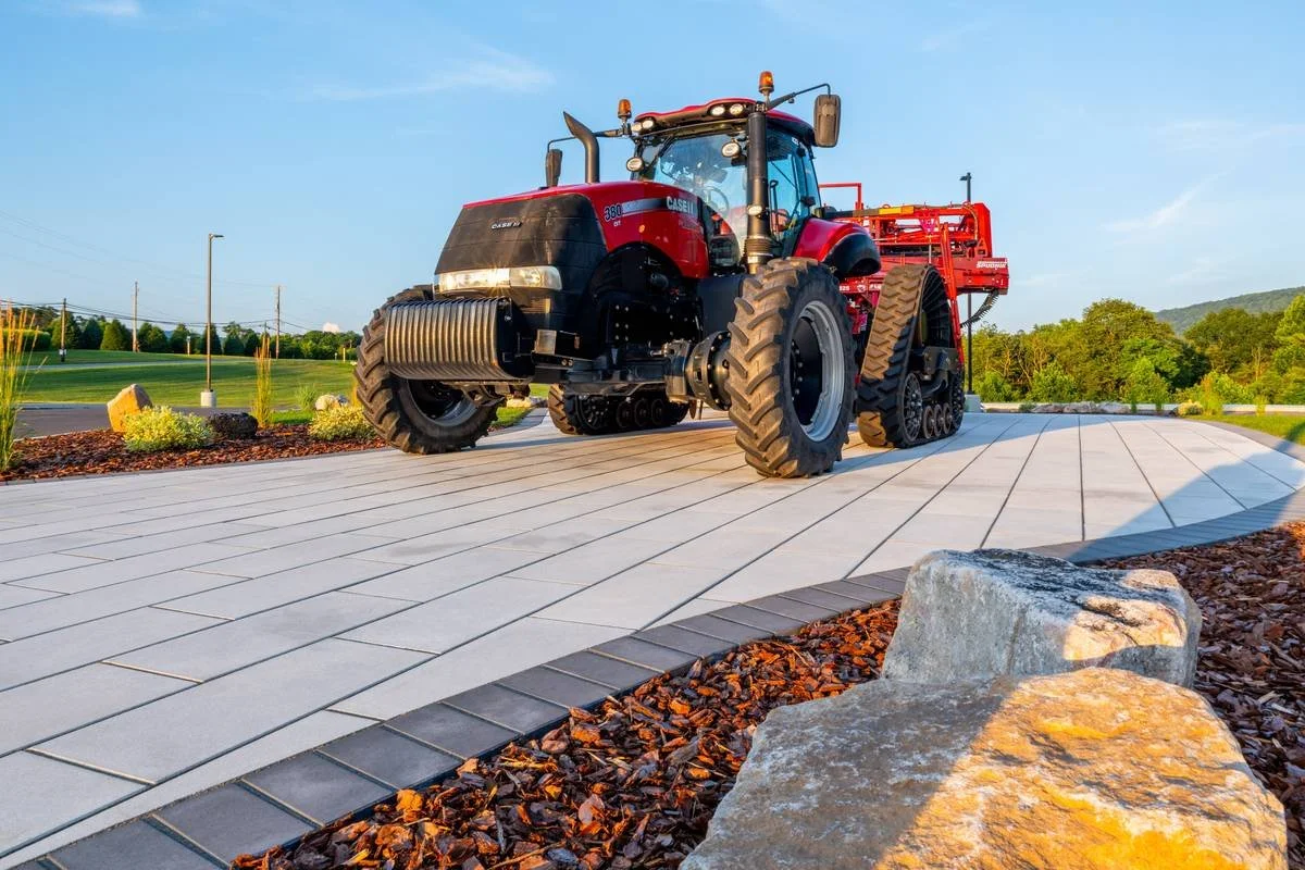 Tractor on a paver display beside a boulder outcropping and pine bark mulch bed — GoldGlo Landscapes