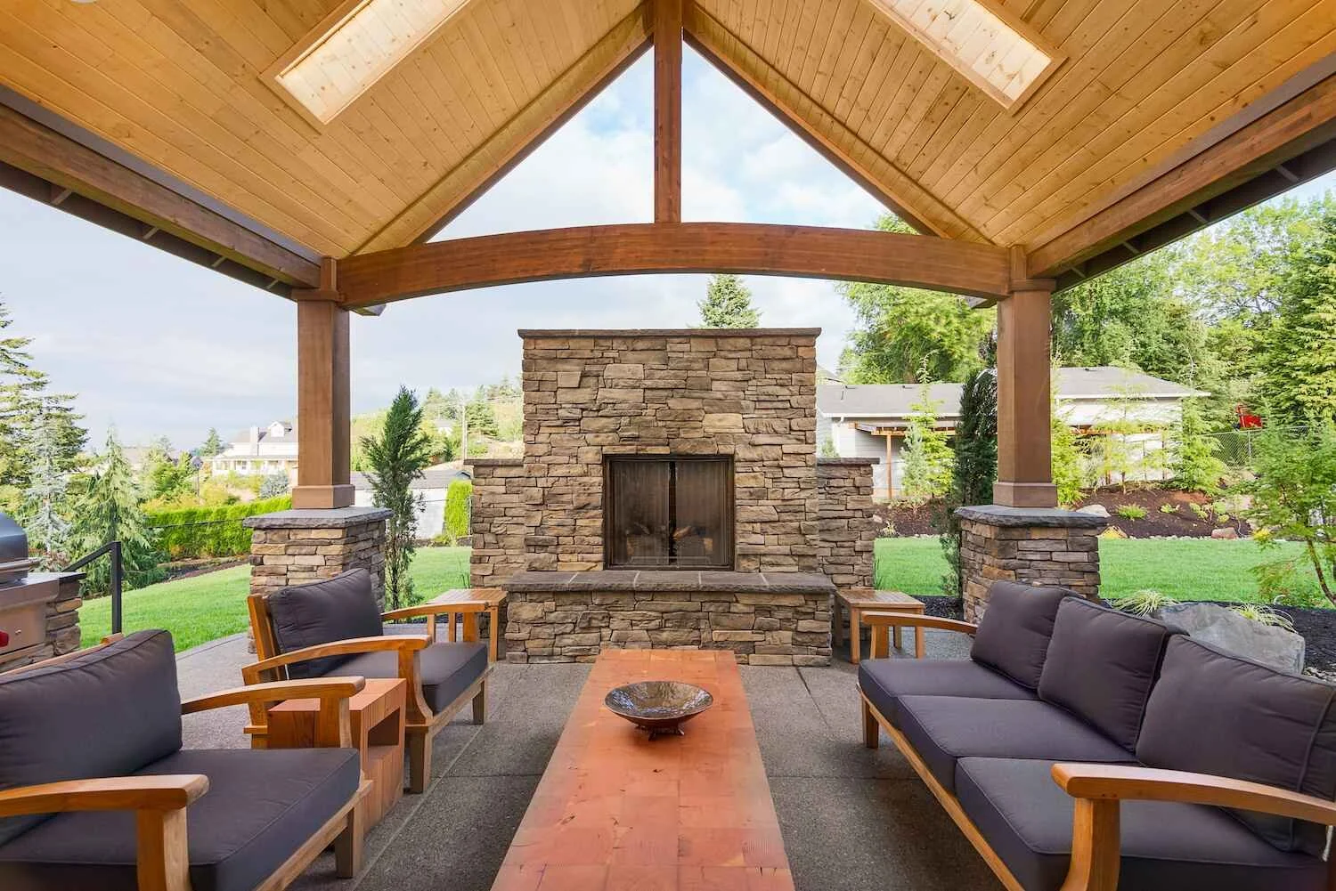 An outdoor fireplace and seating area underneath a wooden pavilion in Westchester County, NY