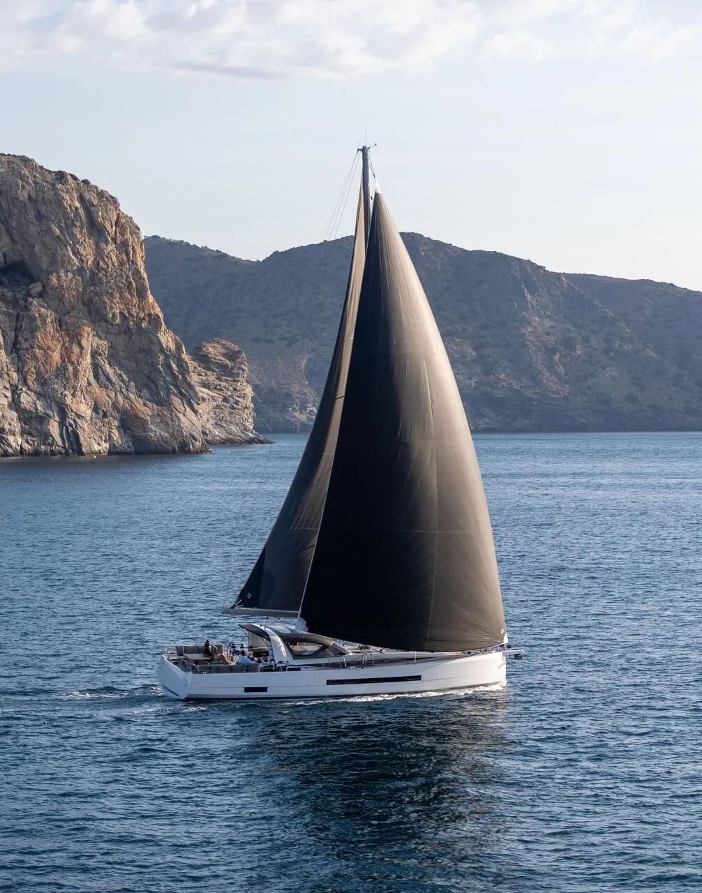 Sailboat with black sails on the ocean near rocky cliffs.