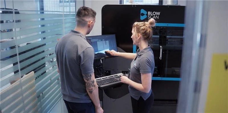 Two people operating a large Blow Scan machine in a modern office or laboratory setting.