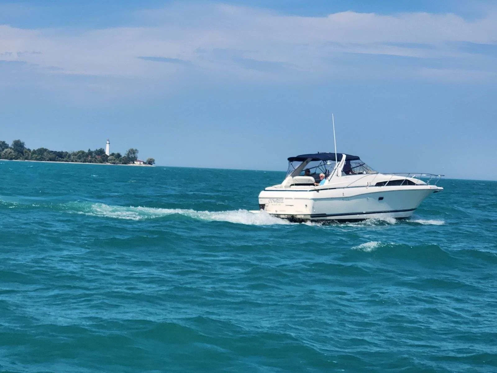 Motorboat on blue water with distant shoreline and lighthouse
