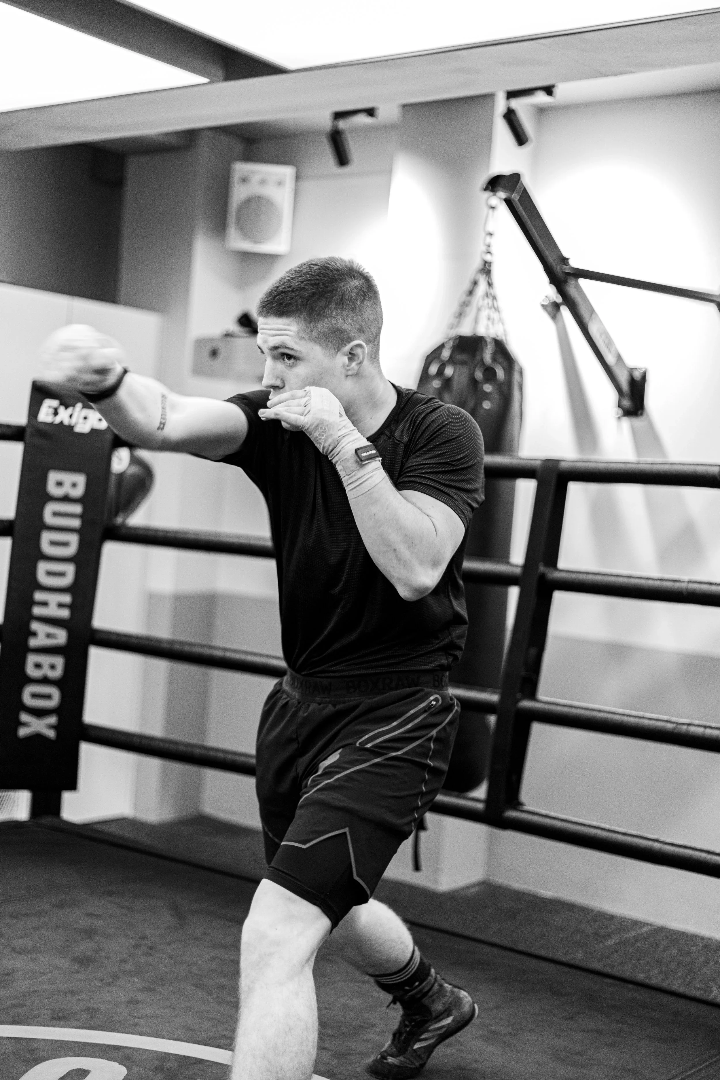 A young man in athletic clothing practicing boxing in a gym, throwing a punch in a ring.