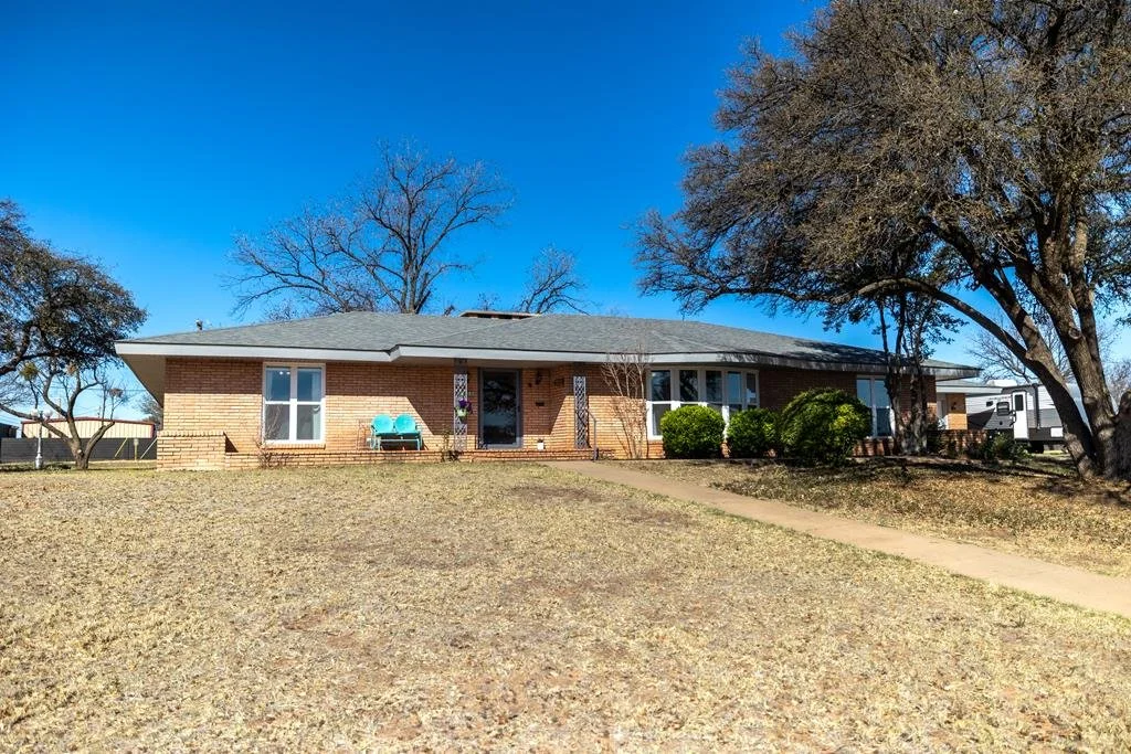 Single-story brick house with a gray roof, large front yard, leafless trees, and a sidewalk leading to the front door.