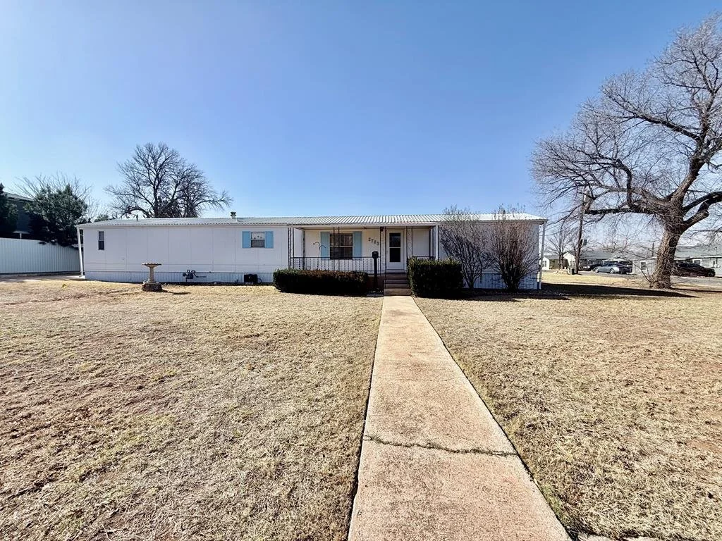 Single-story white house with a front porch, a concrete walkway leading to the front door, bare trees, and a grassy yard under a clear blue sky.