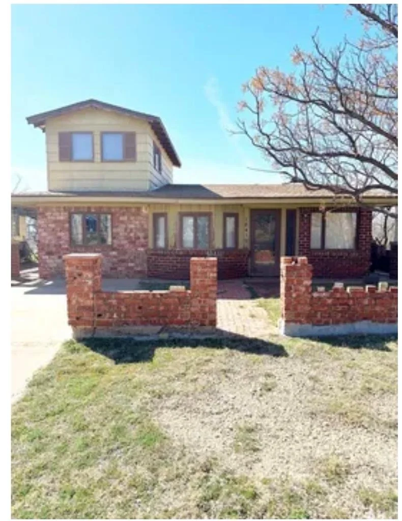 A house with a brick and wood exterior, a small enclosed front yard with a brick wall, and a tree with bare branches in front.