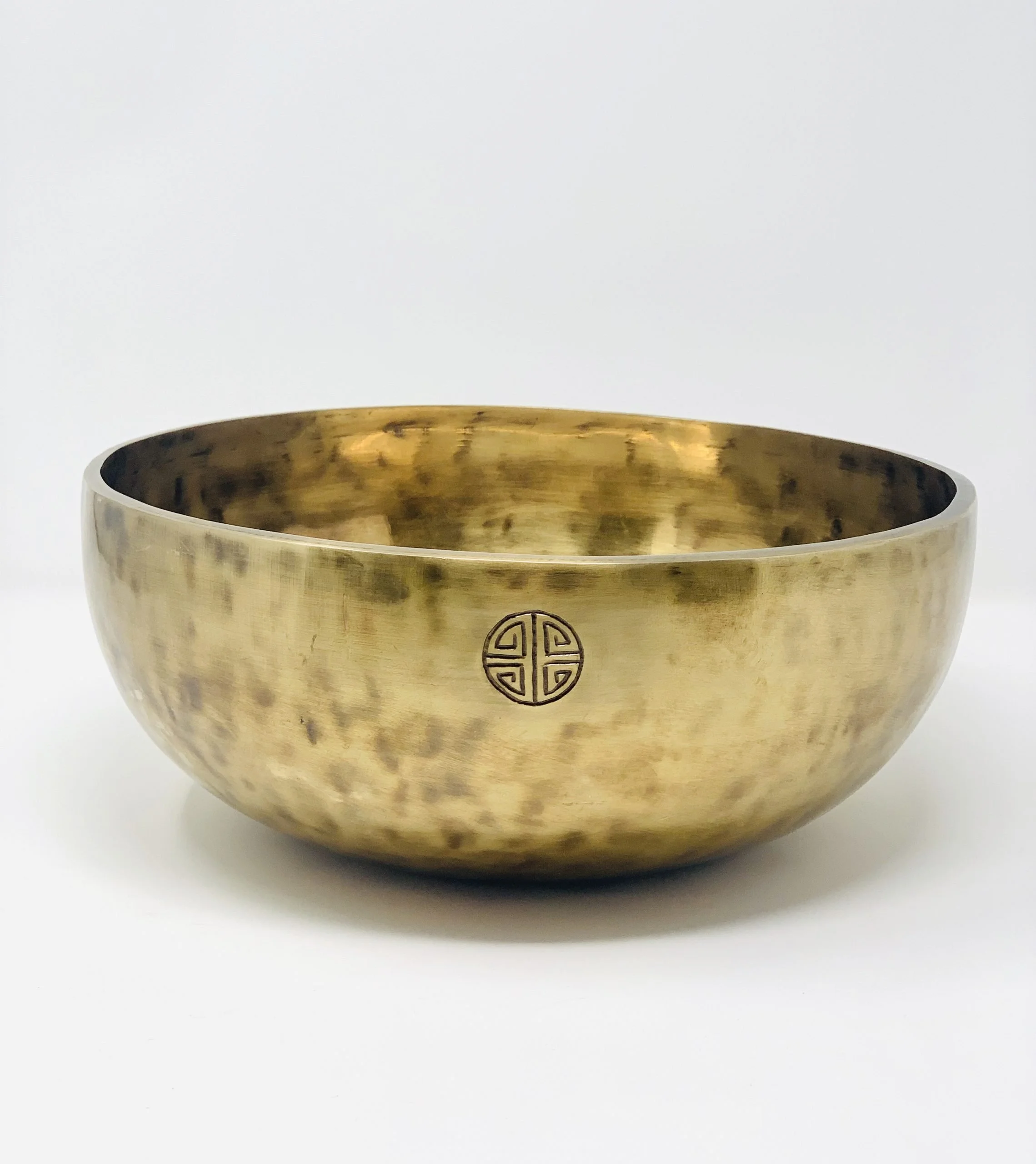 Brass singing bowl with an intricate pattern on the side, placed against a white background.