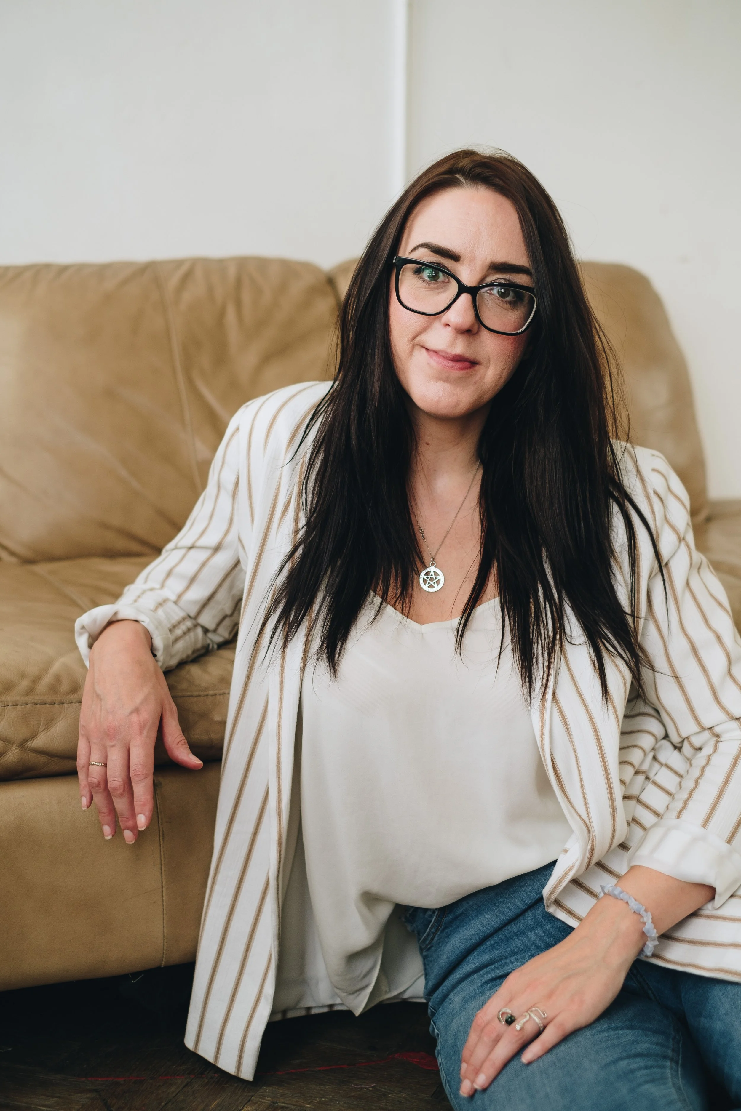 women with long dark hair wearing a cream stripped blazer and black framed glasses looking into the camara