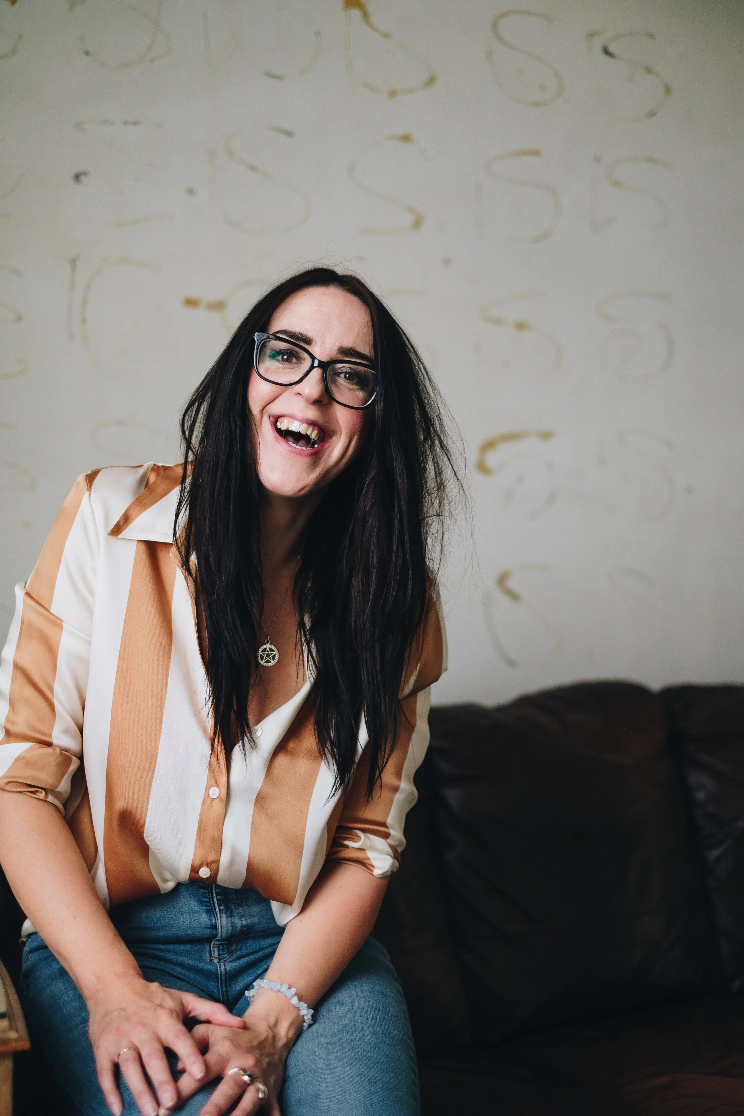 A women with long dark hair who is laughing and wearing glasses
